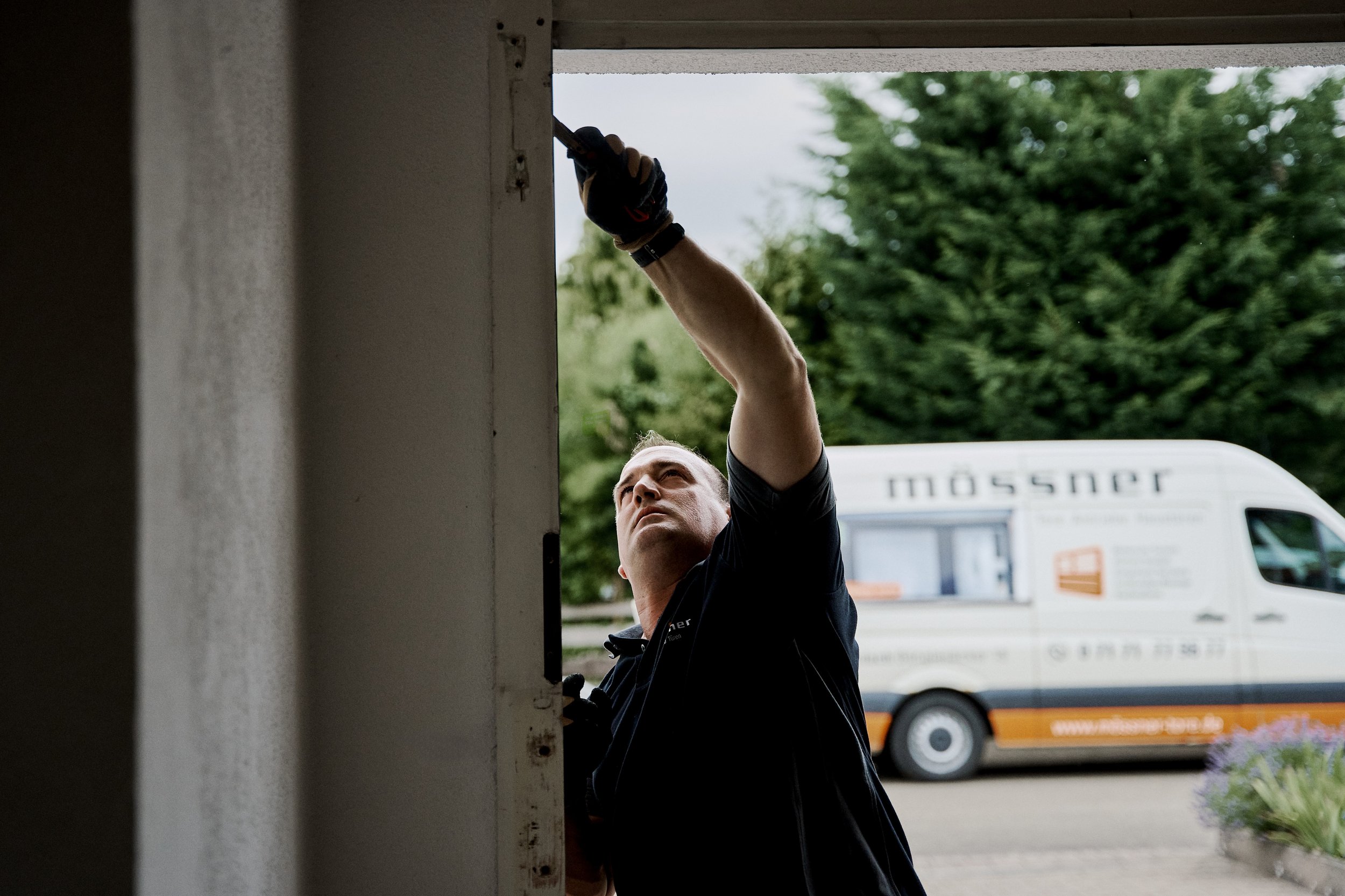 Ein Mann arbeitet an einem Fenster, während er draußen steht. Er trägt schwarze Handschuhe und eine schwarze Jacke.