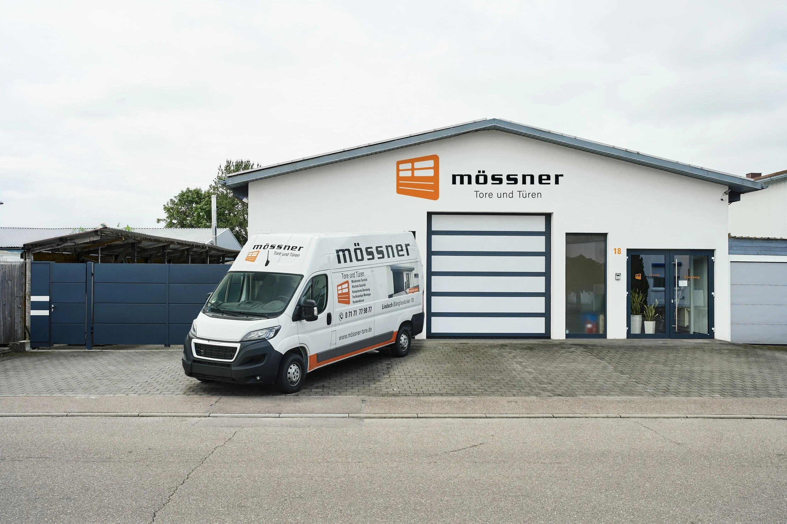 Außenansicht eines Gebäudes mit Firmenbeschilderung und Firmenfahrzeug der Firma Mössner, spezialisiert auf Tore und Türen, in einer industriellen Umgebung.