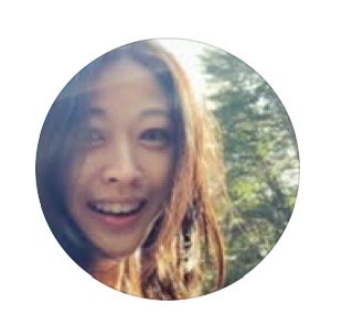 A young woman smiling outdoors with trees and sunlight in the background.