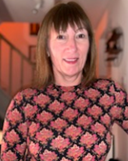 A woman with shoulder-length brown hair wearing a floral patterned top, smiling indoors.
