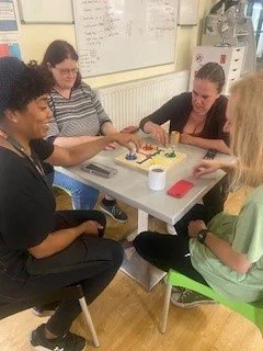 Four women sitting around a table playing a board game in a classroom or activity room.