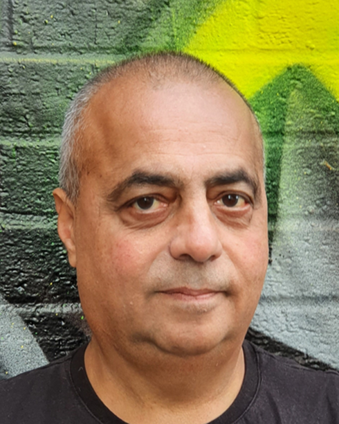 A man with a bald head and dark eyes standing in front of a colorful graffiti wall.