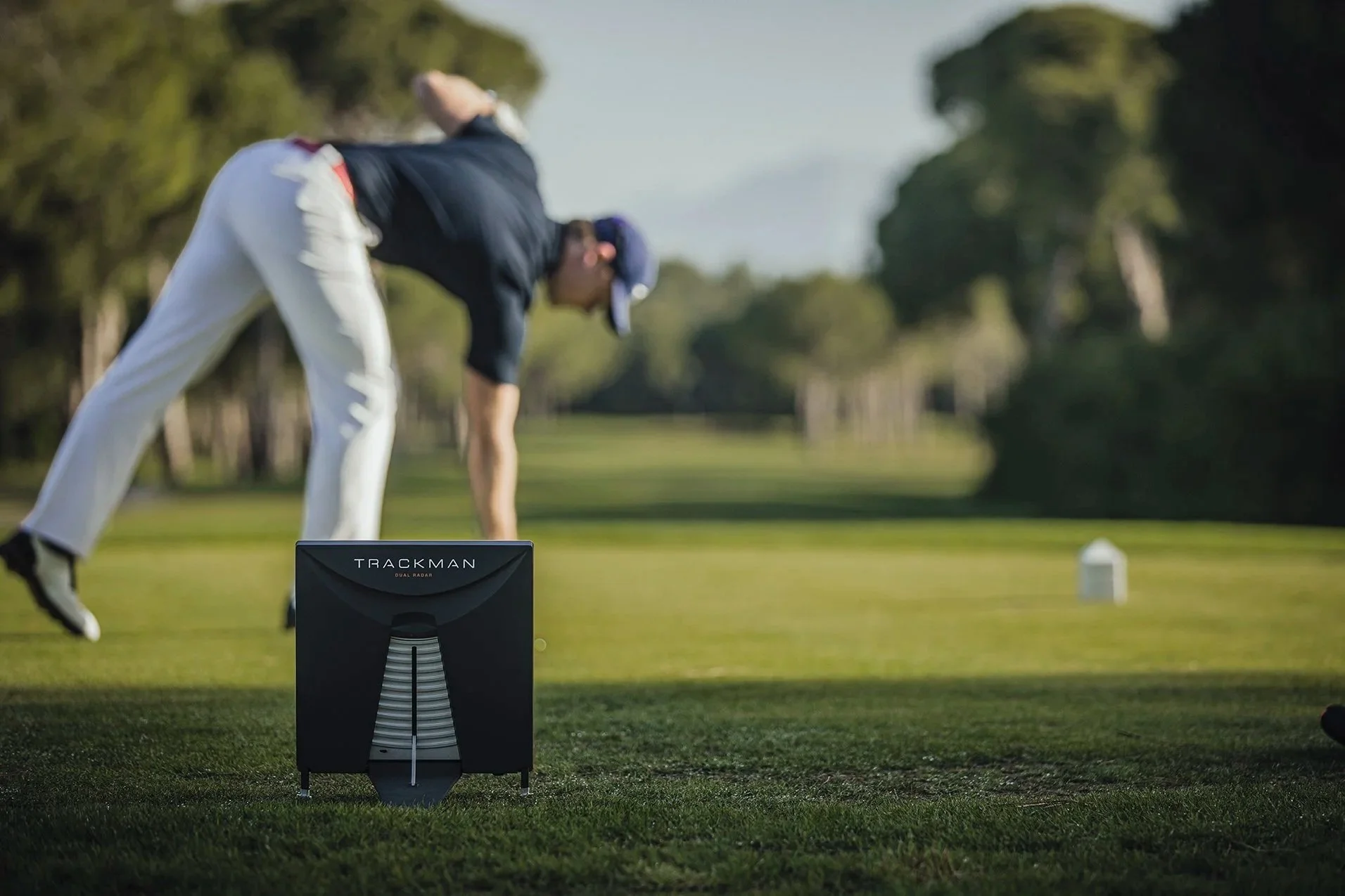 Een man op een golfbaan die zich voorbereidt om te slaan, met een golfbal en een Swing Caddie draagbare golfmeter in de voorgrond.