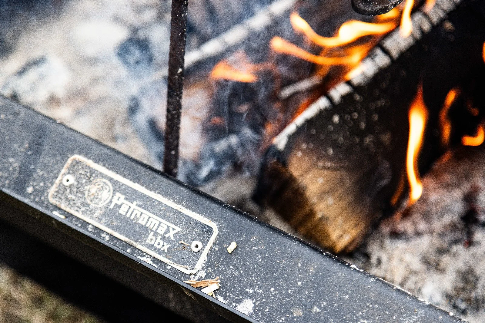 Close-up of a fire burning inside a metal grill with a label that reads 'firebox box', showing blackened metal and orange flames.