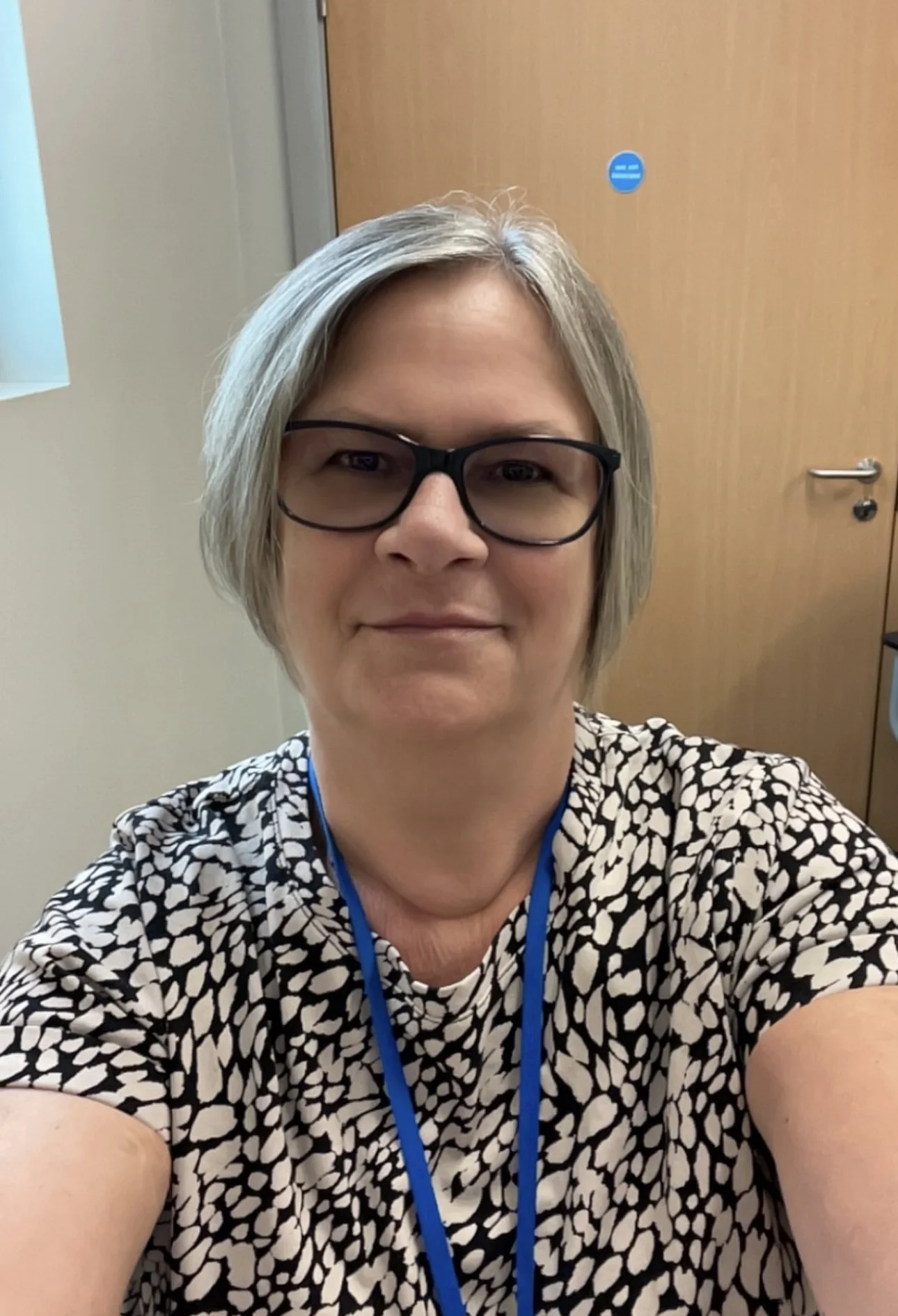 A woman with short gray hair and glasses taking a selfie in front of a wooden door.