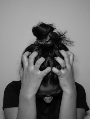 Person with hair in a bun holding their head with both hands, face down, in black and white.