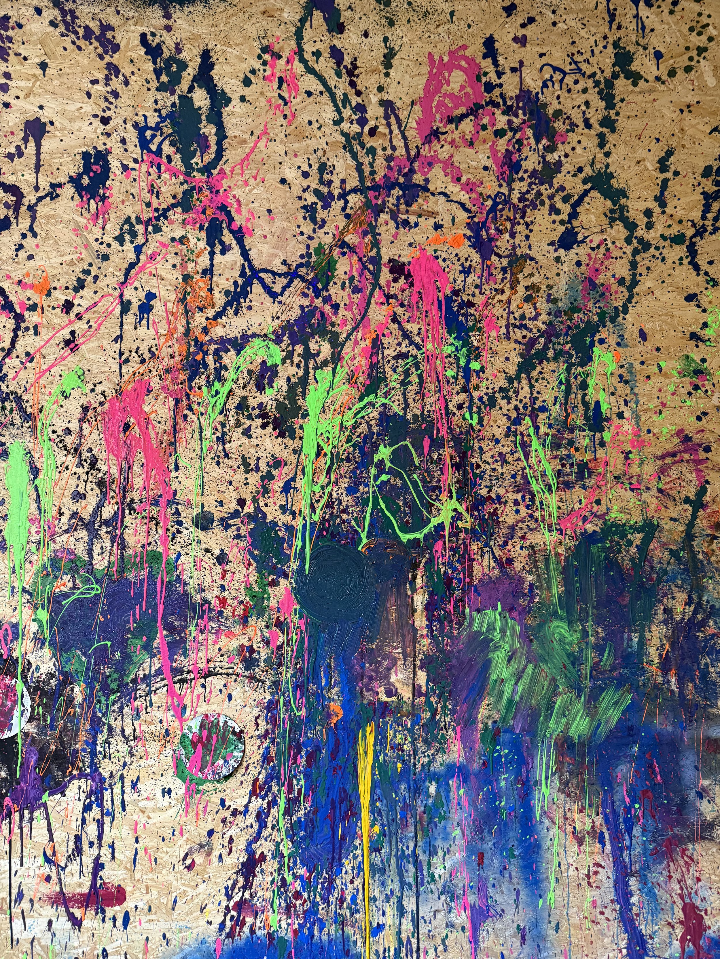Abstract splatter painting with vibrant neon colors on a wooden background.