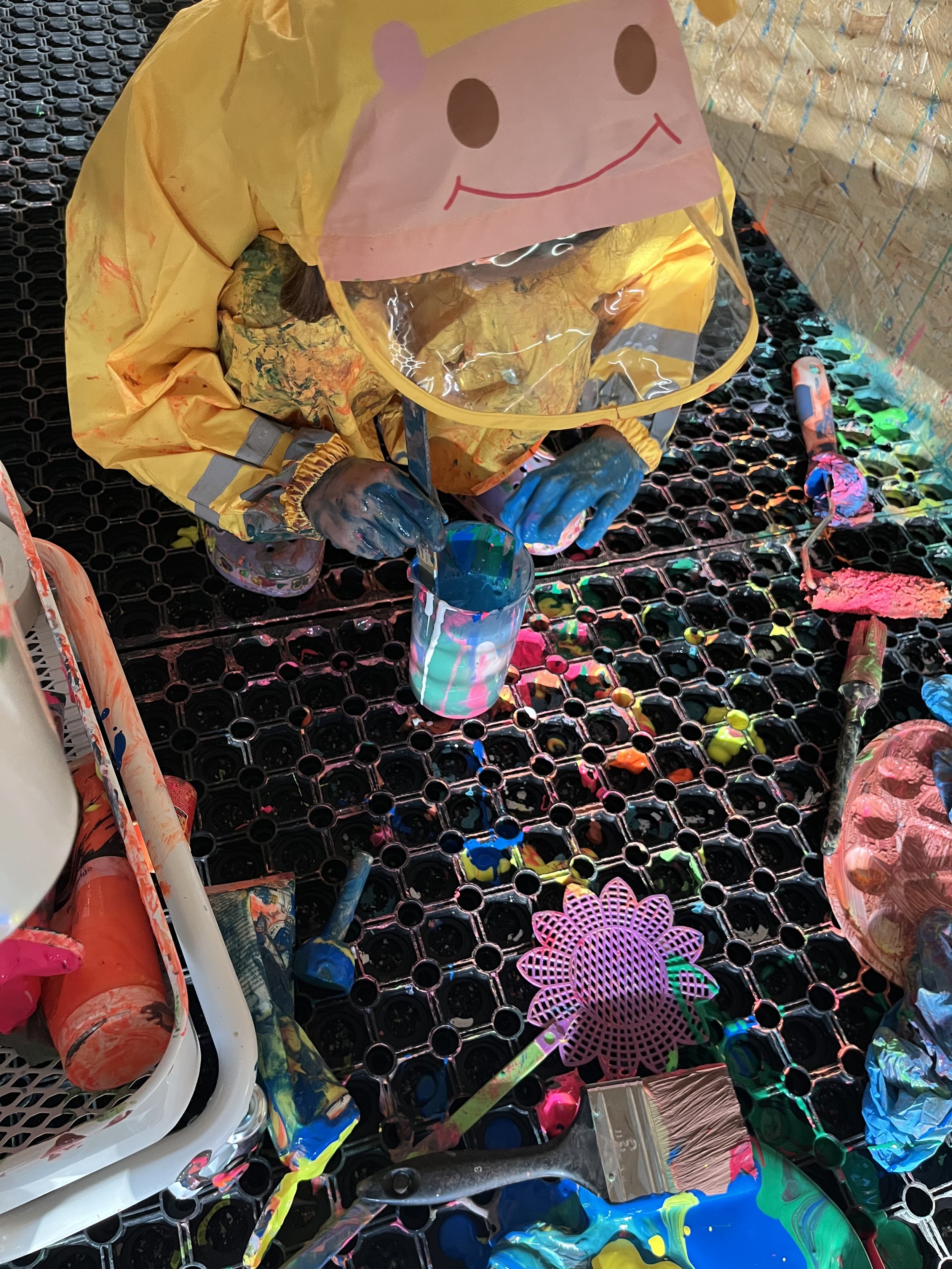 A child's artwork creating a colorful scene with paint, brushes, and a paper mask with a smiling face.