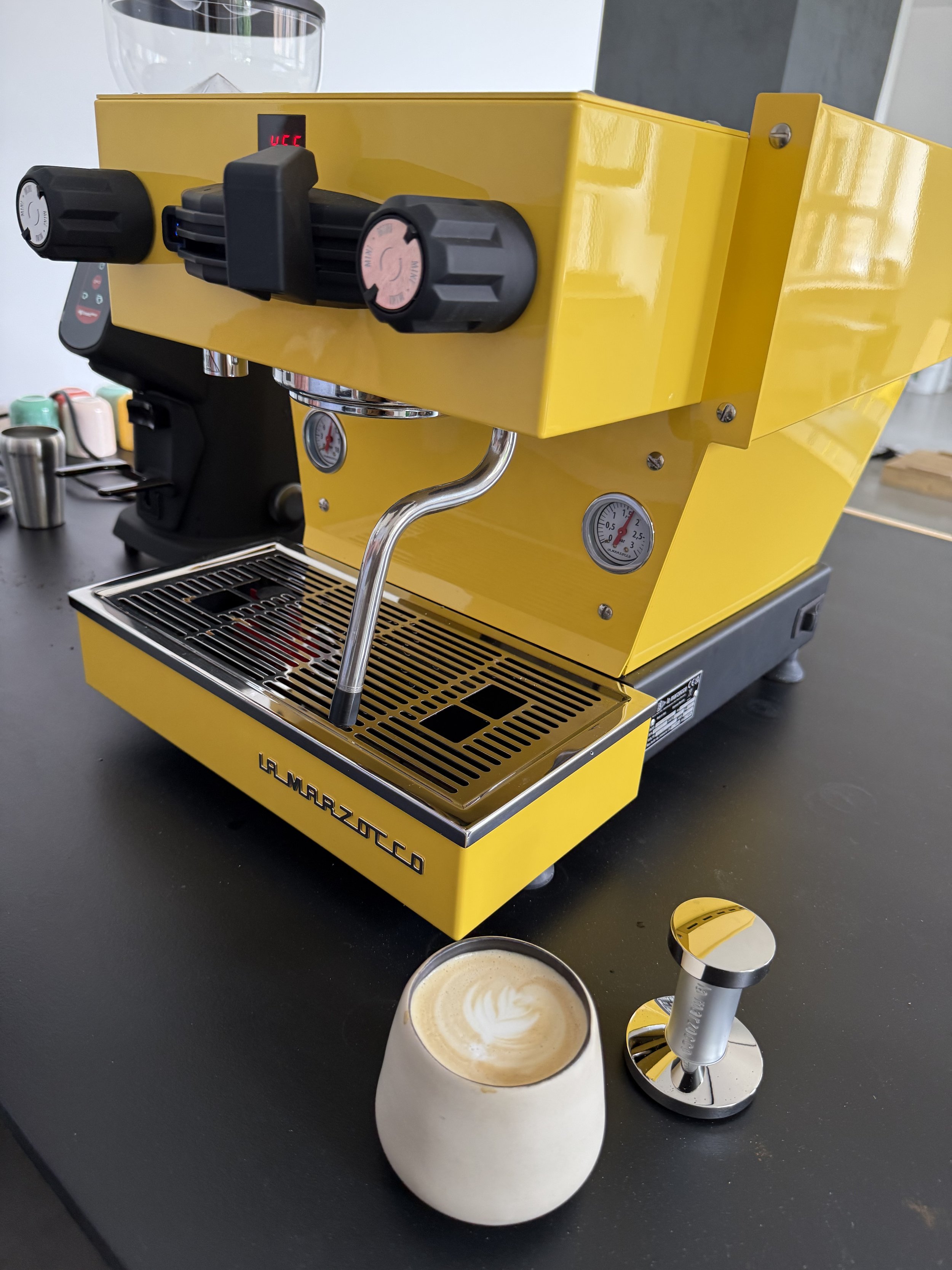 Yellow espresso machine with two cups of coffee and a portafilter on a black counter.