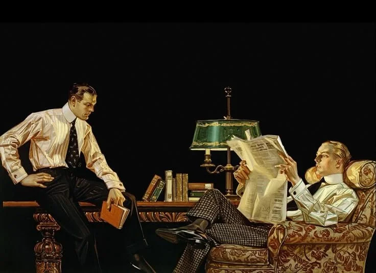 Two men in vintage business attire in an office setting, one seated in a patterned armchair reading a newspaper and the other standing holding a book, with a desk, books, and a green-shaded lamp between them.