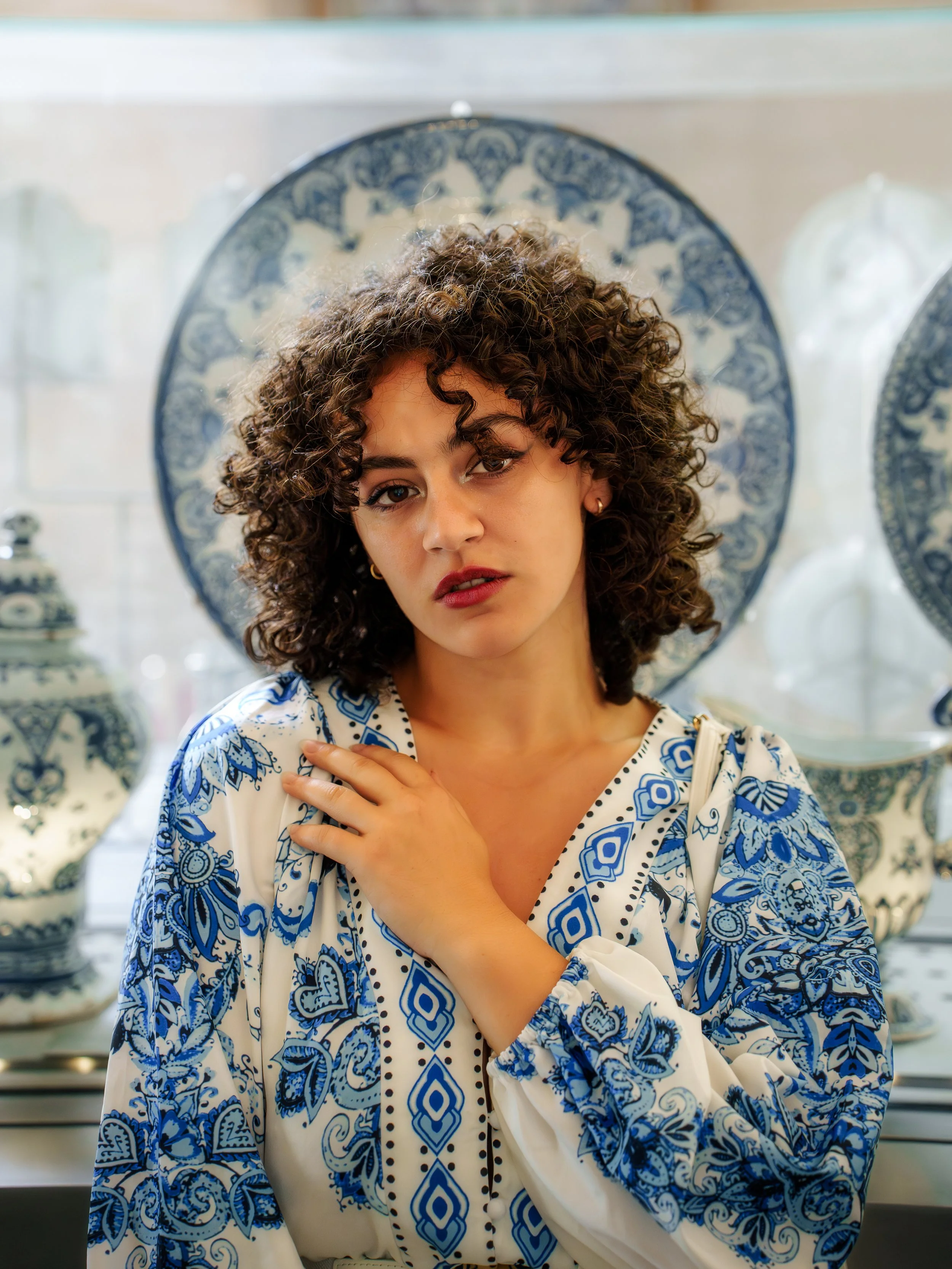 Jeune femme aux cheveux bouclés portant une robe blanche et bleue avec un décor en porcelaine en arrière-plan.