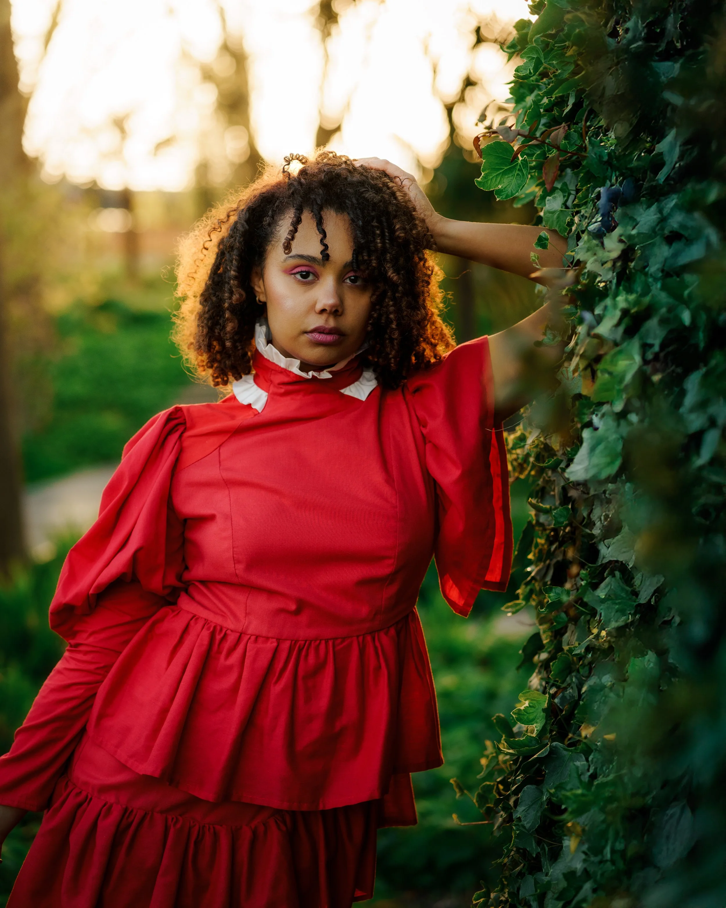 Femme avec des cheveux bouclés en robe rouge dans un jardin entourée de verdure.