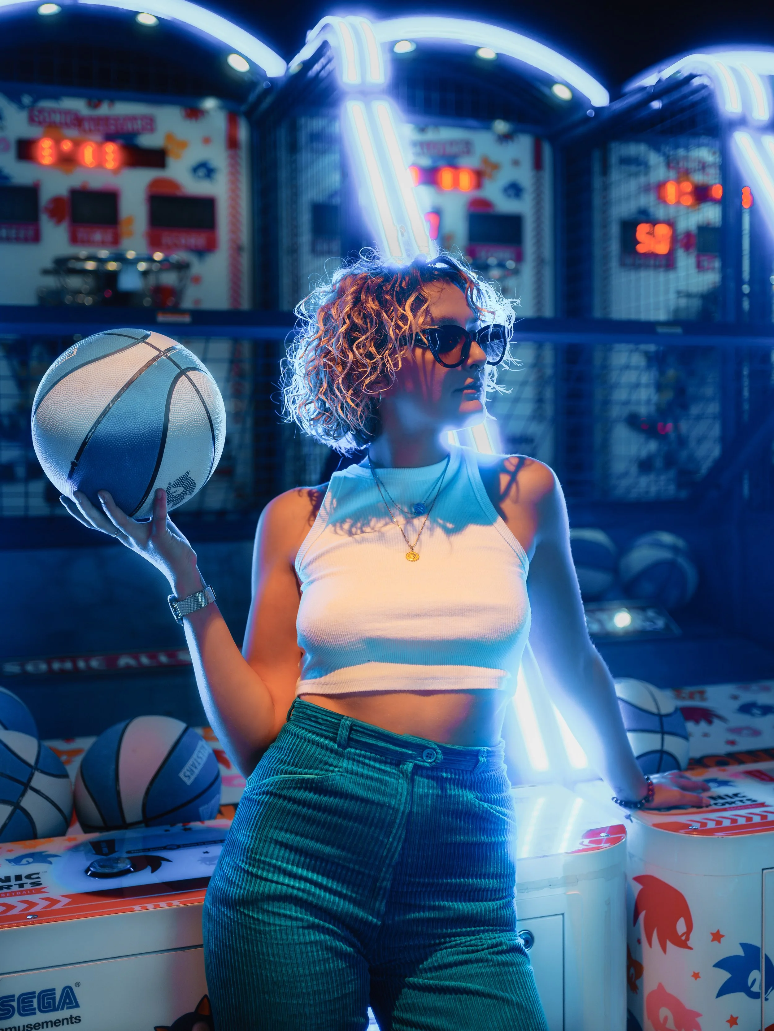 Jeune femme jouant au basket dans une arcade avec néons bleus et décor coloré.