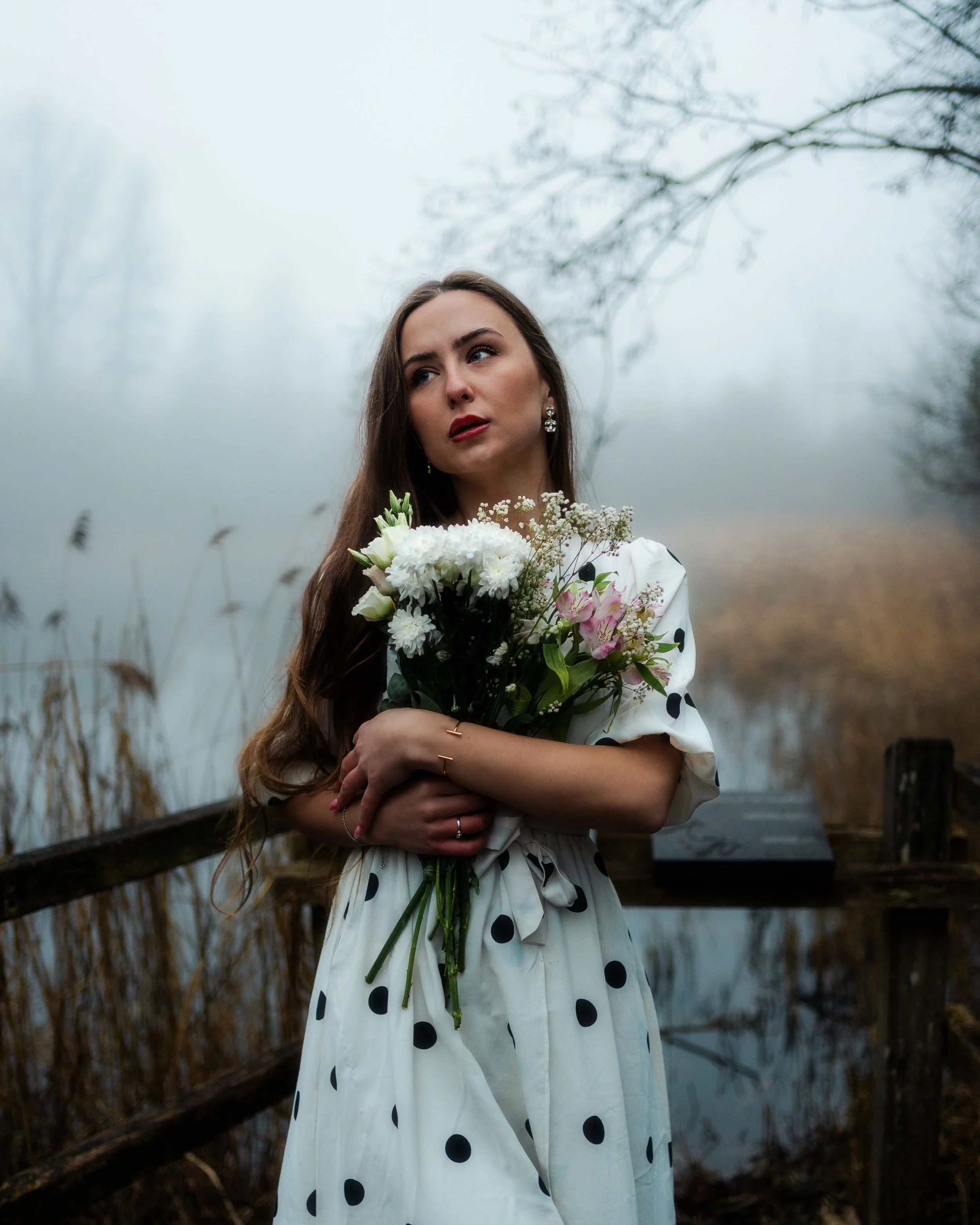 Une femme tenant un bouquet de fleurs à côté d'un étang brumeux dans un environnement naturel