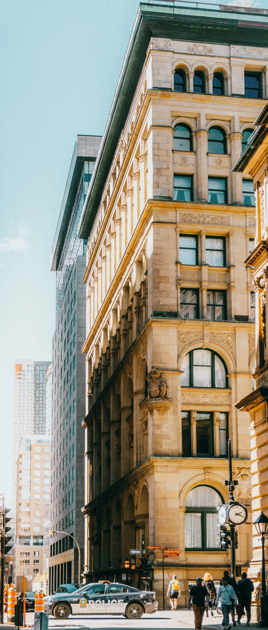 Bâtiment historique avec architecture ancienne, situé en centre-ville, avec des personnes marchant devant et une voiture de police à l'avant.