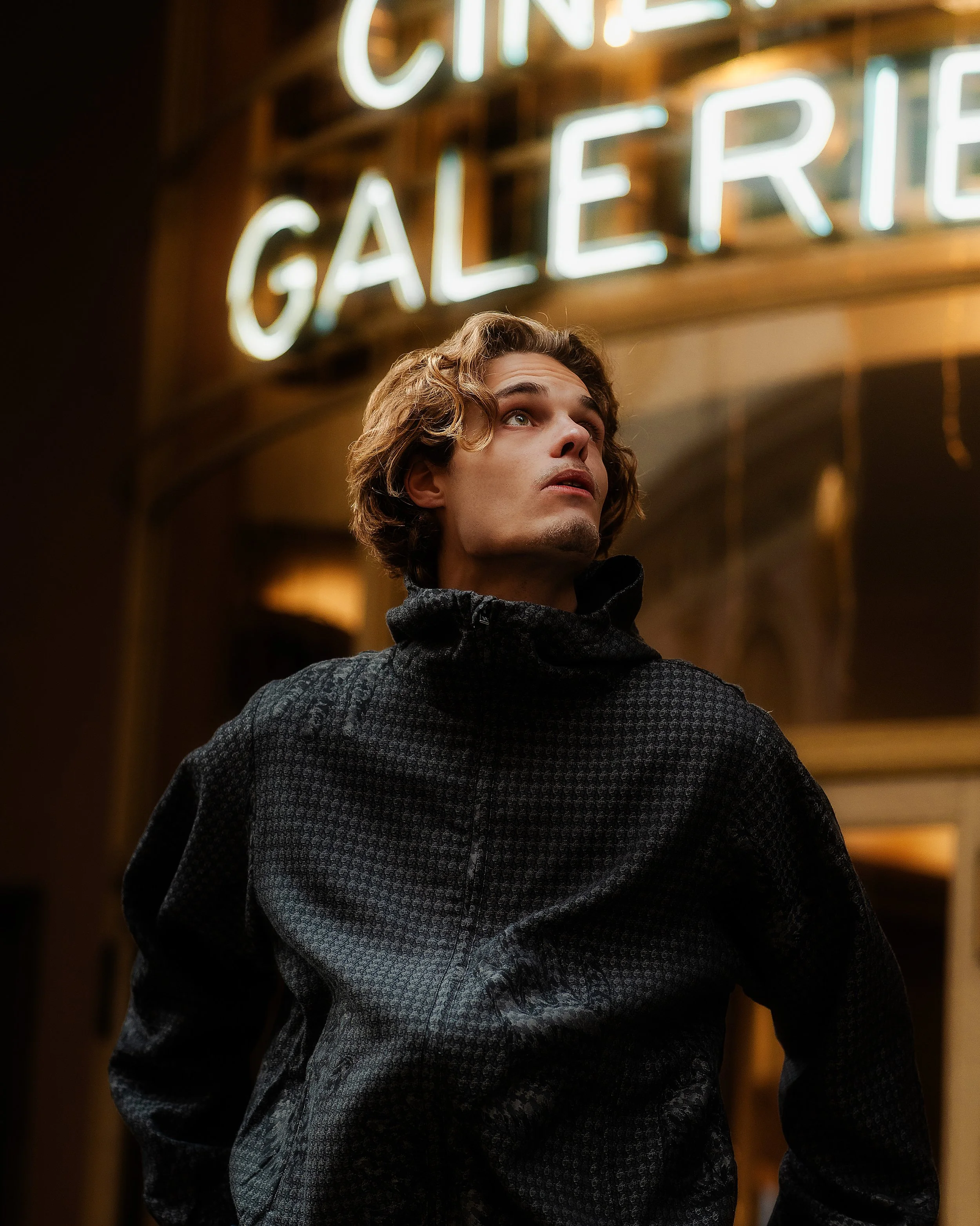 Jeune homme regardant vers le haut devant un panneau lumineux 'Cité Galerie'