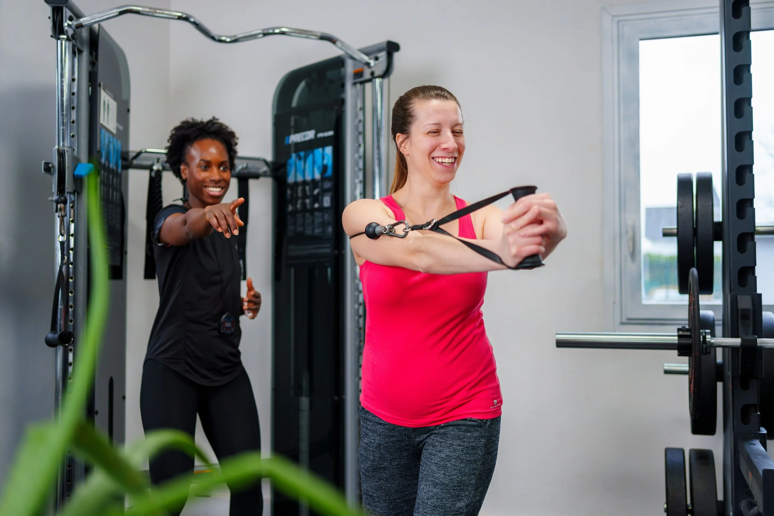 Deux femmes font de l'exercice en salle de sport. L'une utilise une bande de résistance, l'autre lui donne des encouragements.