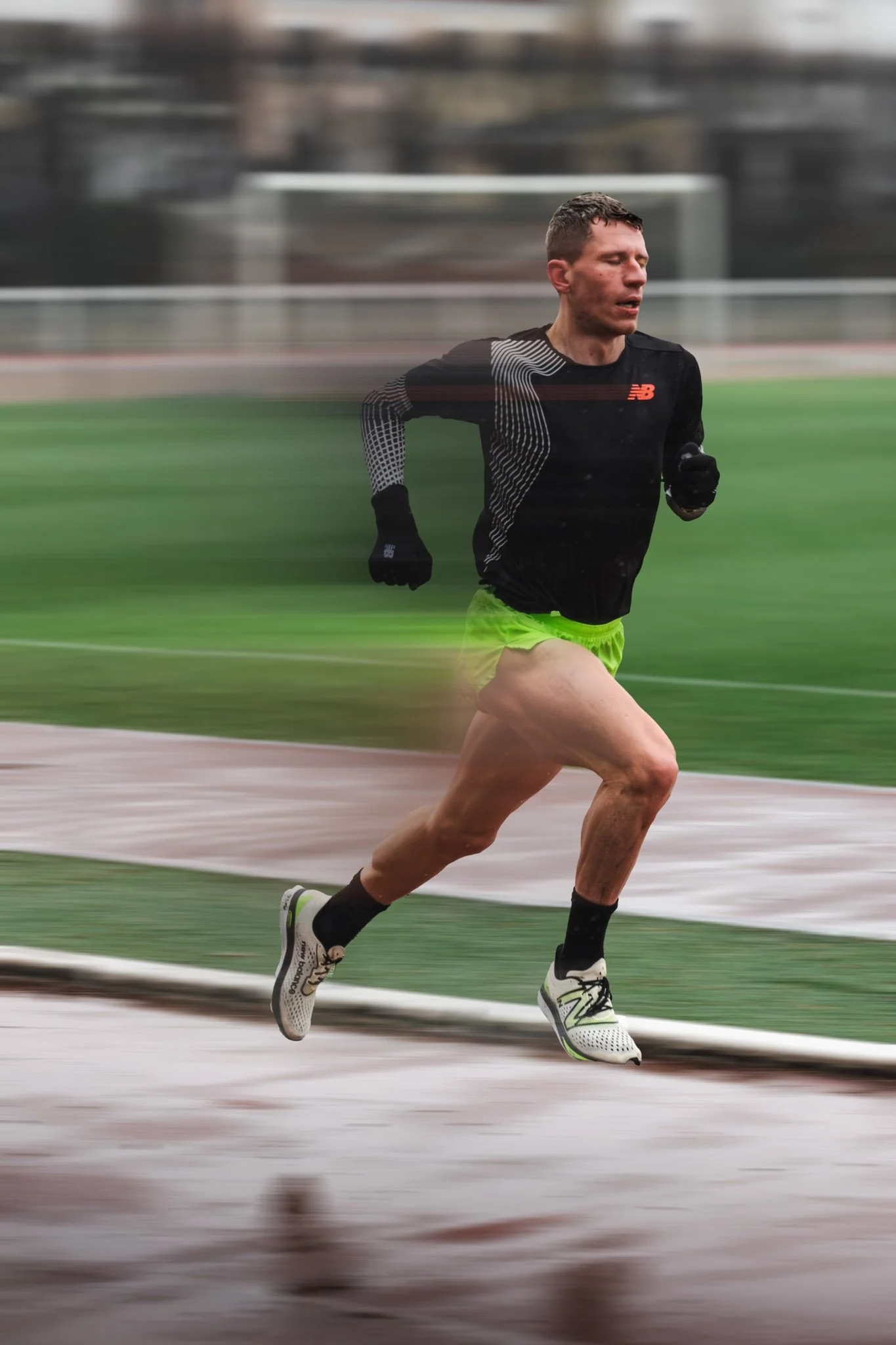 Un homme court sur un terrain d'athlétisme, portant un maillot noir et des shorts verts, avec un mouvement de vitesse lui créant une traînée floue derrière lui.