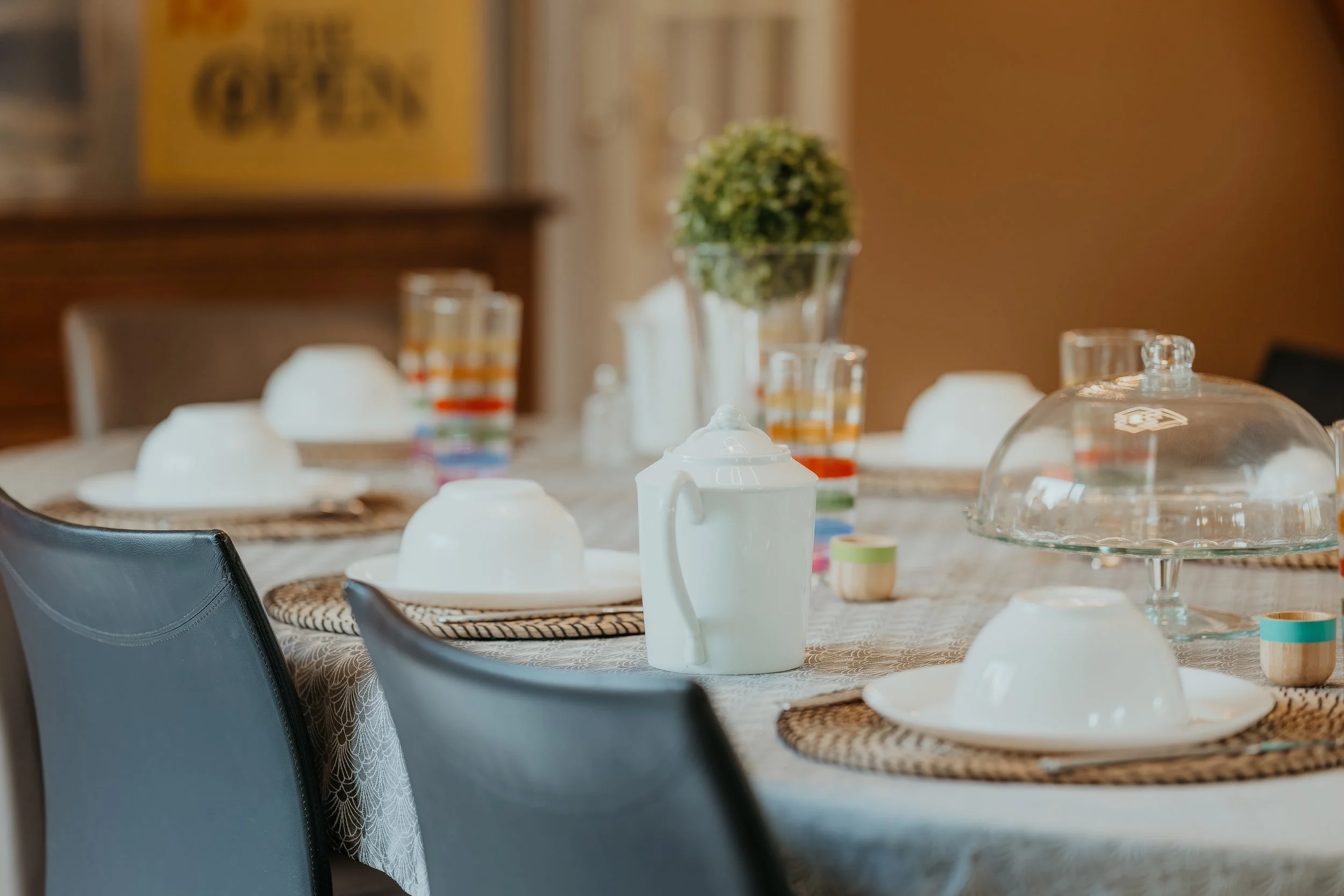 Table de dîner préparée avec assiettes, verres, nappe, et un centre de table avec une plante verte, prête pour un repas