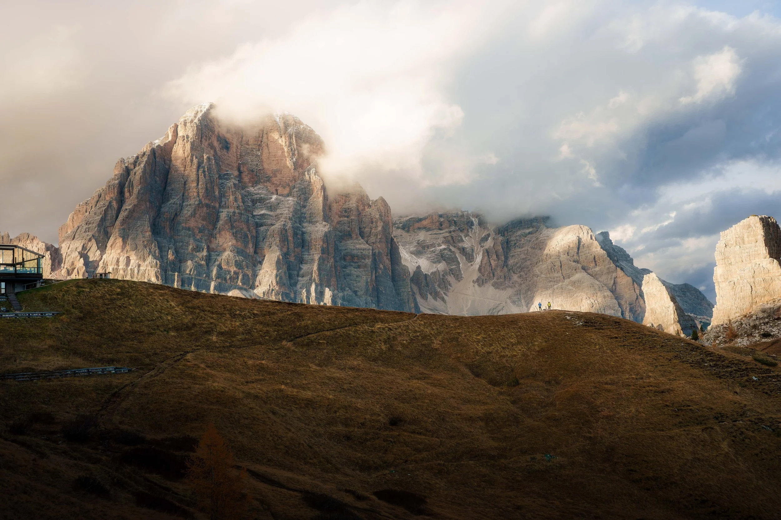 Paysage de montagnes rocheuses avec des nuages partiellement couvrant le sommet, et un terrain vallonné en premier plan.