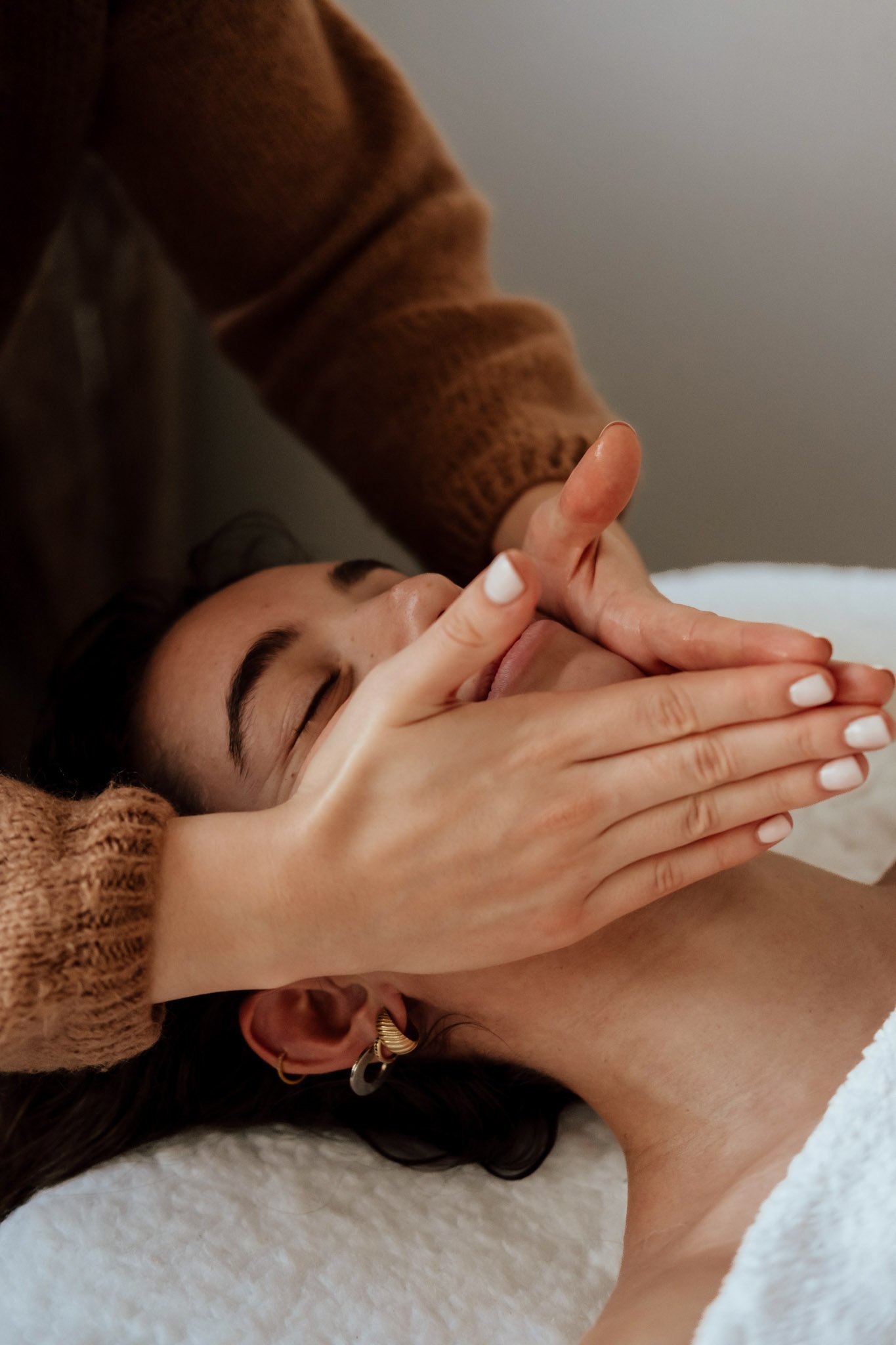 Une femme reçoit un massage du visage par une praticienne dans un cadre relaxant.