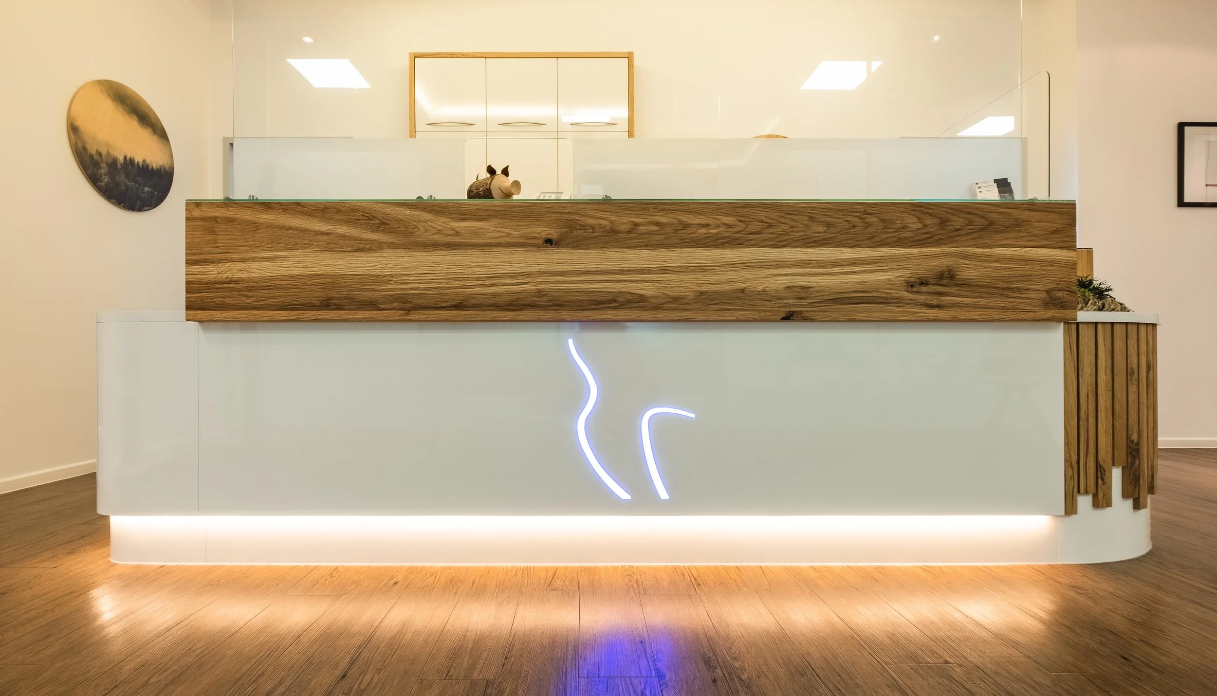 Moderne Empfangstheke mit Holz- und weißen Elementen, LED-Beleuchtung und neonartiger Linie an der Front.