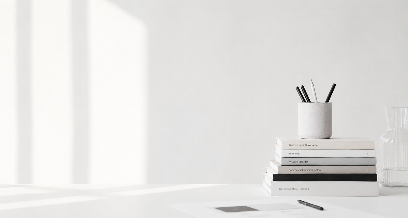 Heller Arbeitsplatz mit viel Weißraum, Designbüchern, Stiften und dezenten Kreativ-Elementen als Symbol für Strategie, Gestaltung und klare Kommunikation.