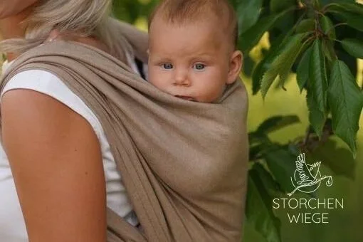 Ein Baby, das auf dem Rücken einer Frau in einem Tragetuch sitzt, vor grünen Blättern.