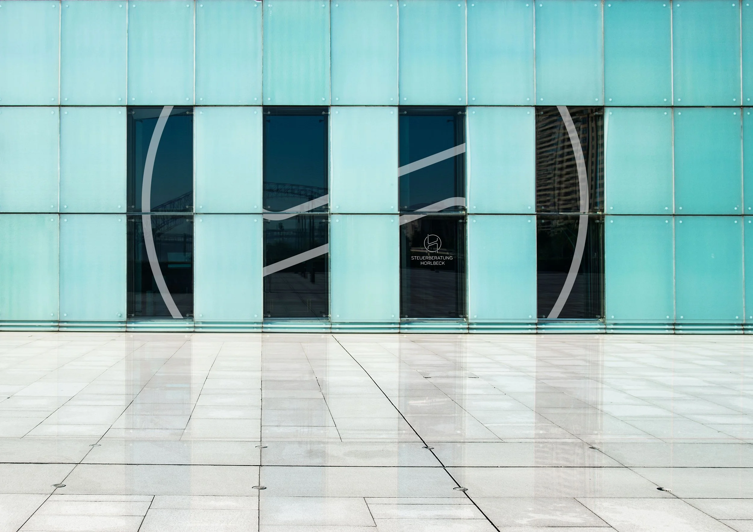 Moderne Glasfassade mit reflektierenden Fenstern und Markierung, die das Unternehmen Steuerberatung Horlbeck anzeigen.