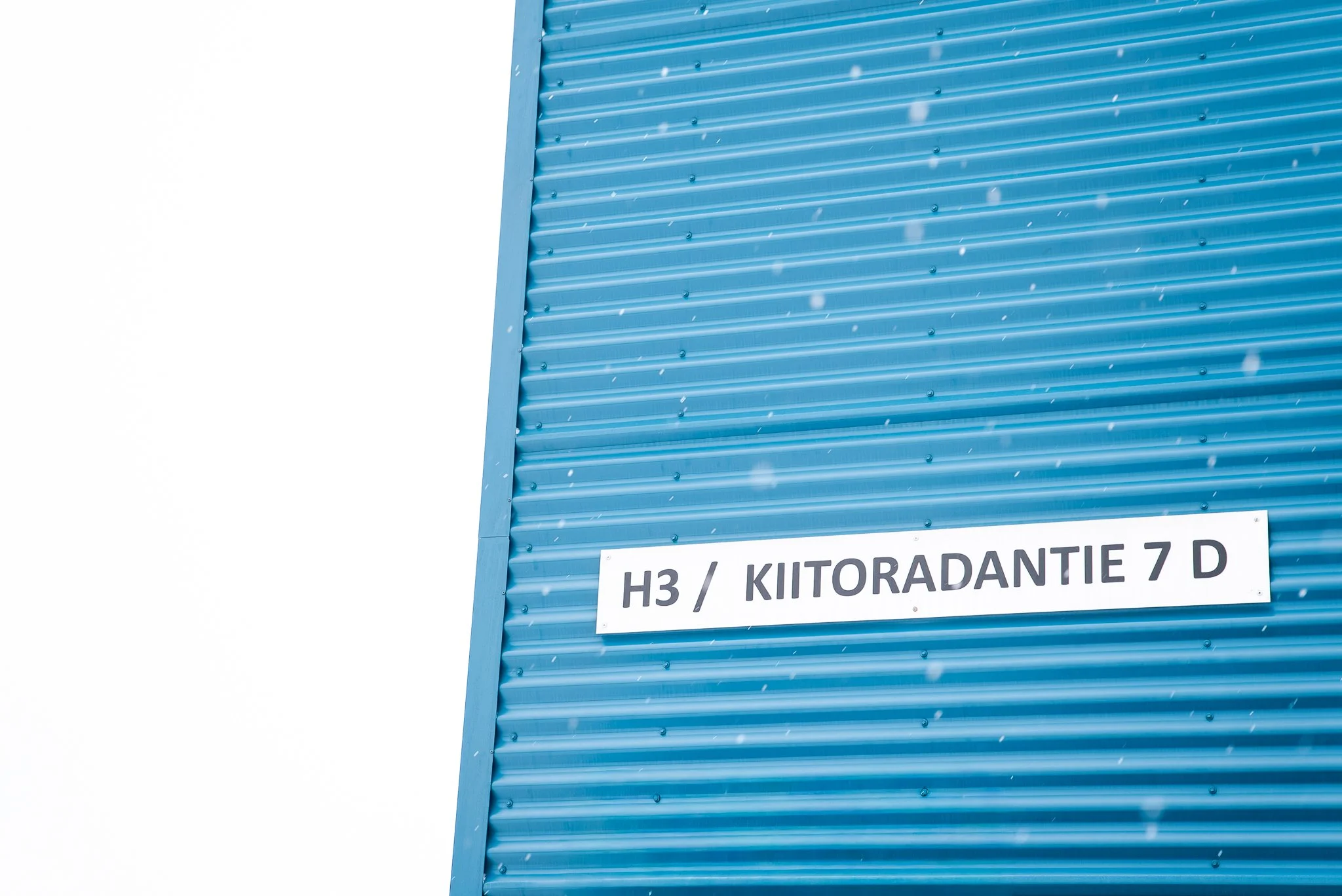 Kirmainen teollisuusrakennus, jossa on moderni sininen metalliseinä, ja siihen on kiinnitetty kyltti, jossa lukee 'H3 / KIITORADANTIE 7 D'.