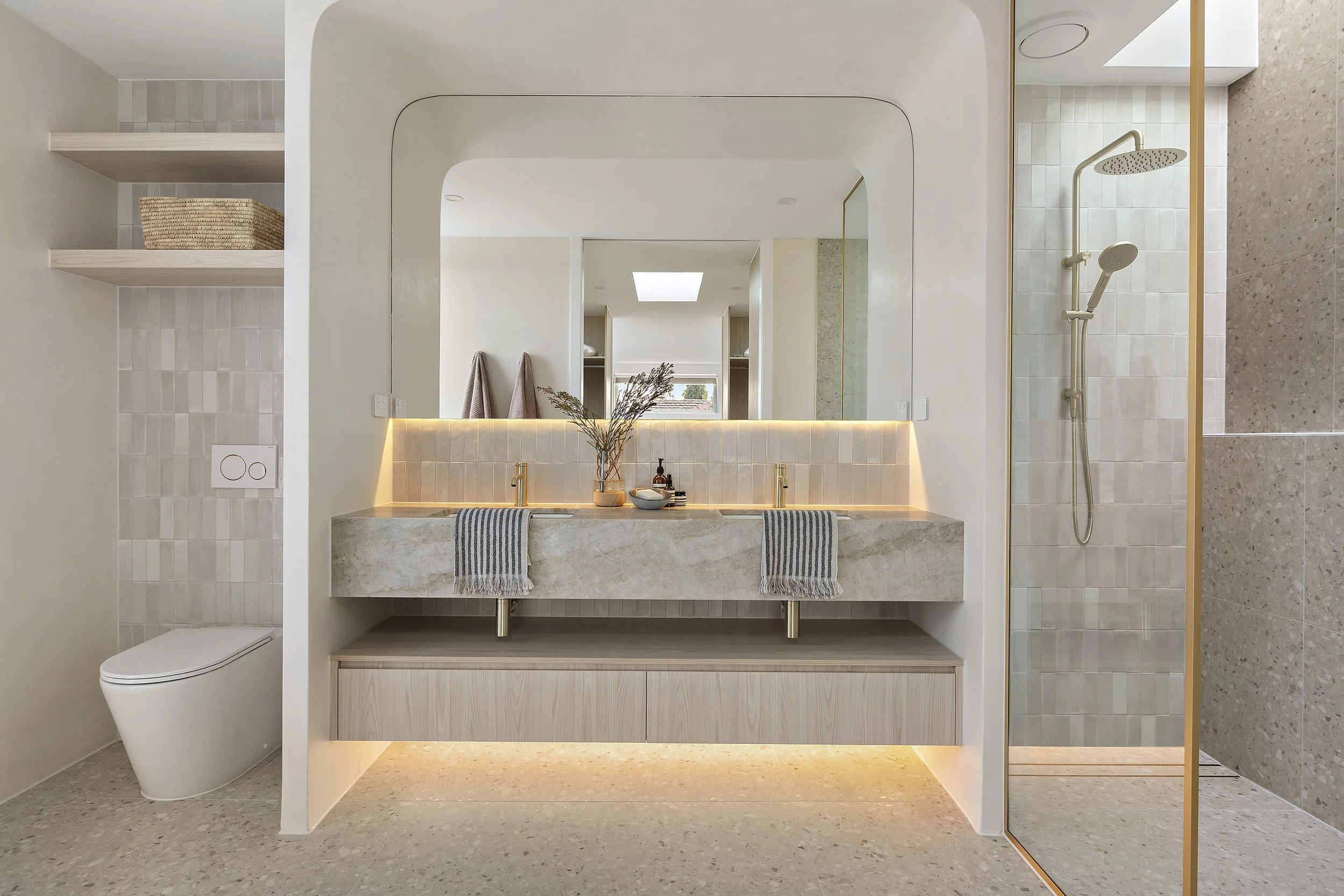 Modern bathroom with a double vanity, large mirror, and walk-in shower, decorated in neutral tones with plants and towels.