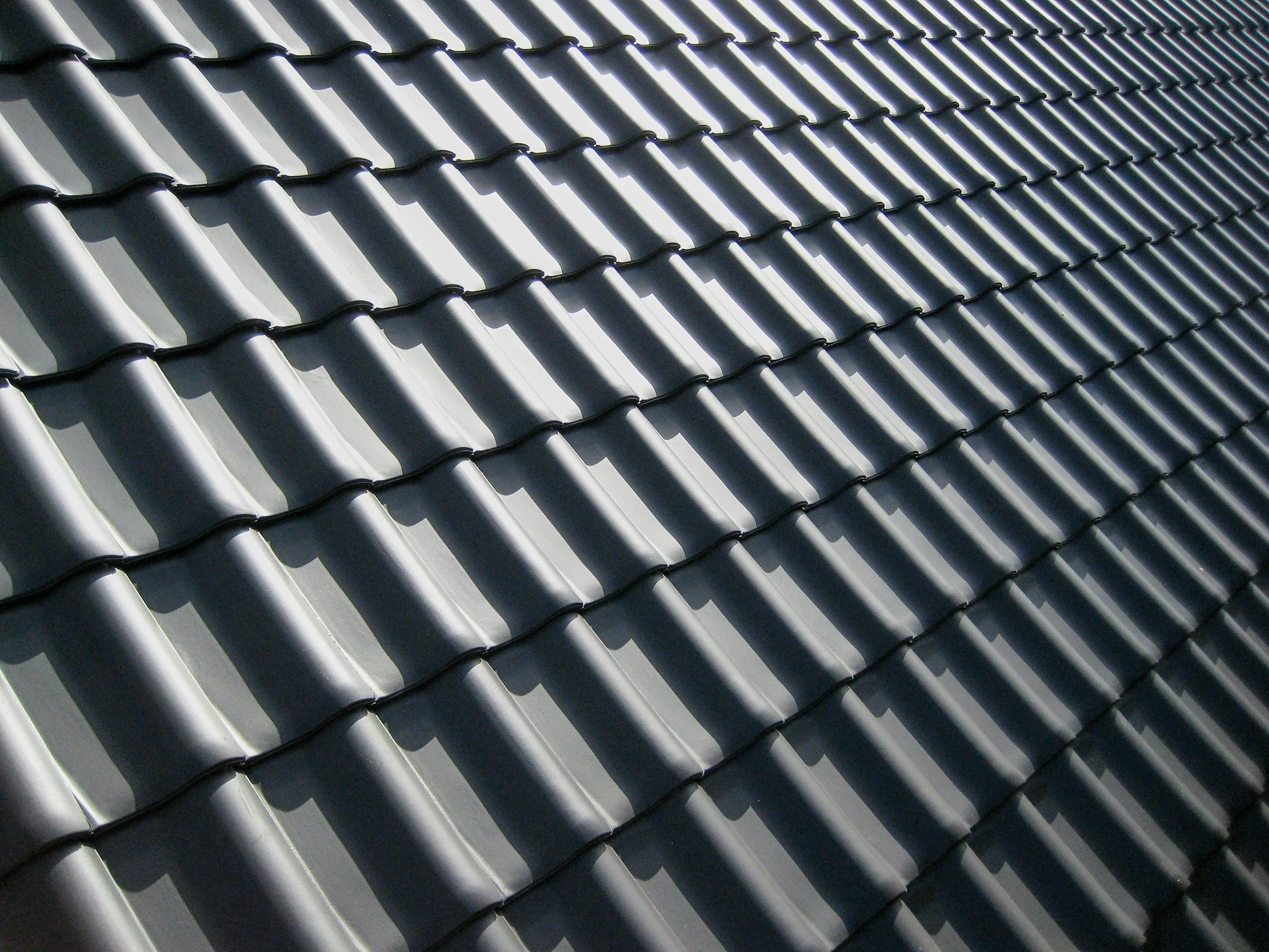 Close-up of a dark gray roof with overlapping curved tiles casting shadows.