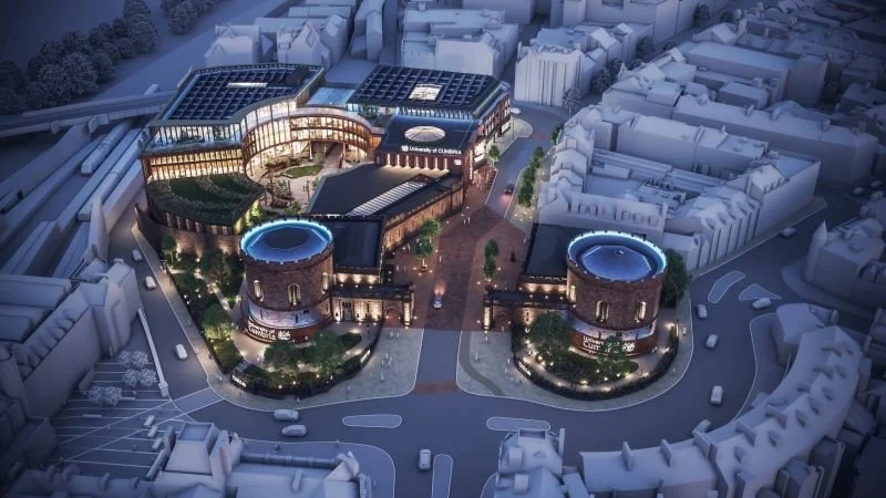 Night view of a modern university campus with illuminated buildings, two round towers with blue roofs, open courtyards, and surrounding city streets.