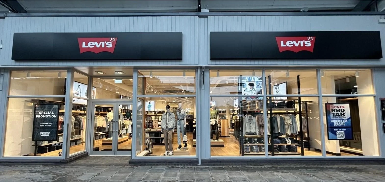 Exterior view of a Levi's store with glass windows showing mannequins dressed in casual clothing. Store signage displays the Levi's logo in red and white.