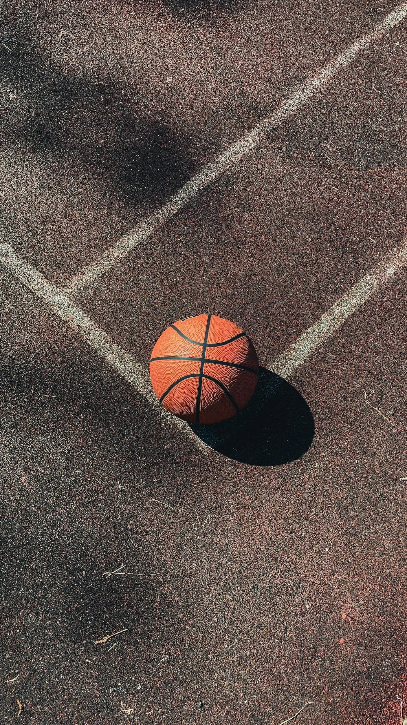 Basketball on outdoor court with white lines and shadows.
