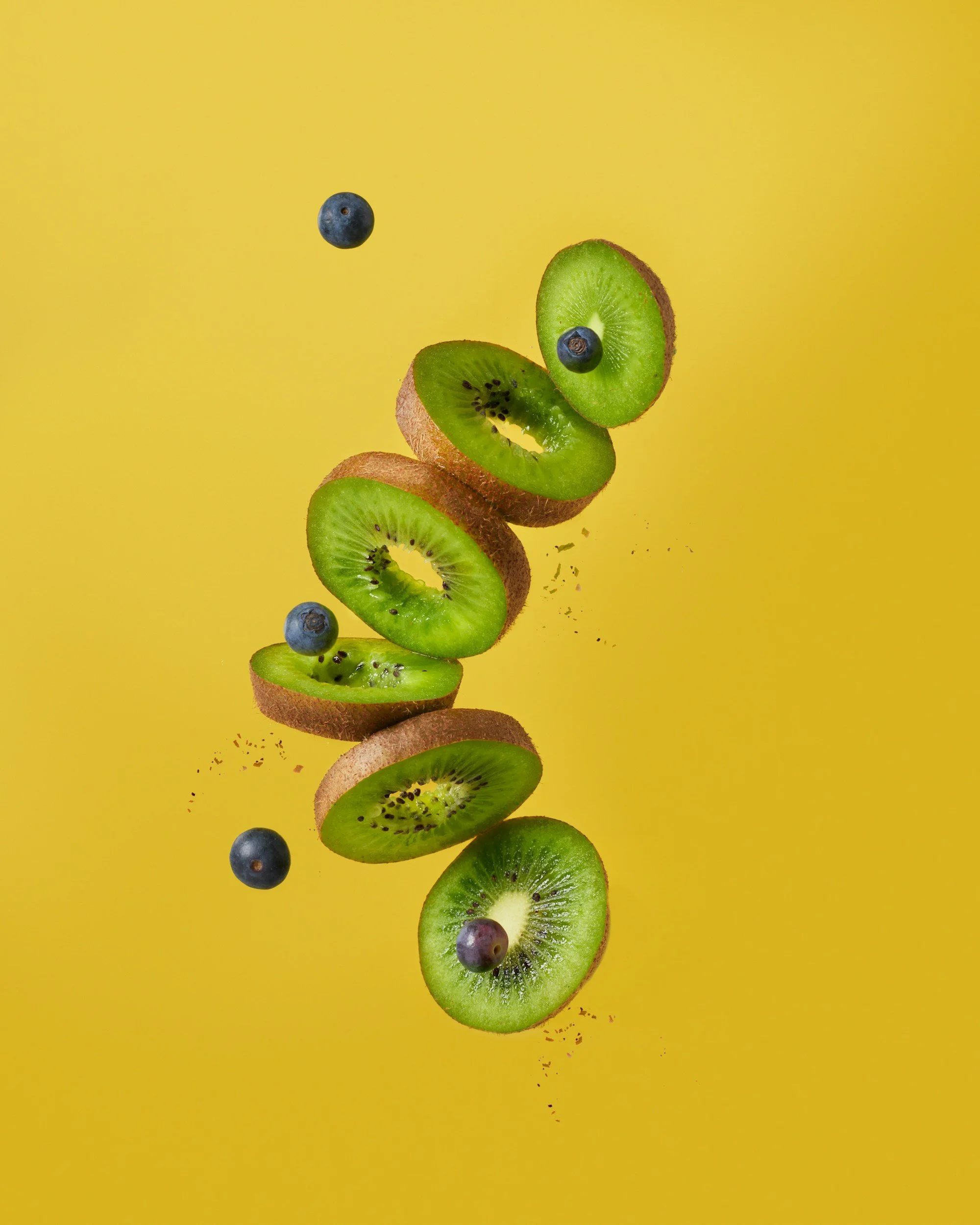 Sliced kiwi and whole blueberries falling against a yellow background.