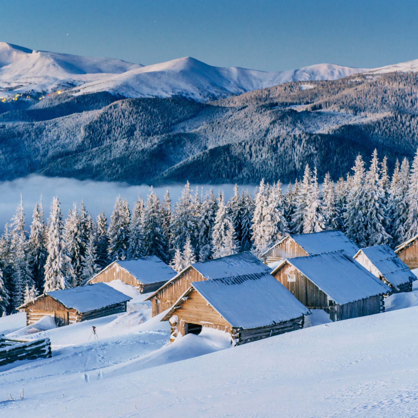 Small alpine chalets with snow-covered roofs surrounded by snowy trees and mountains