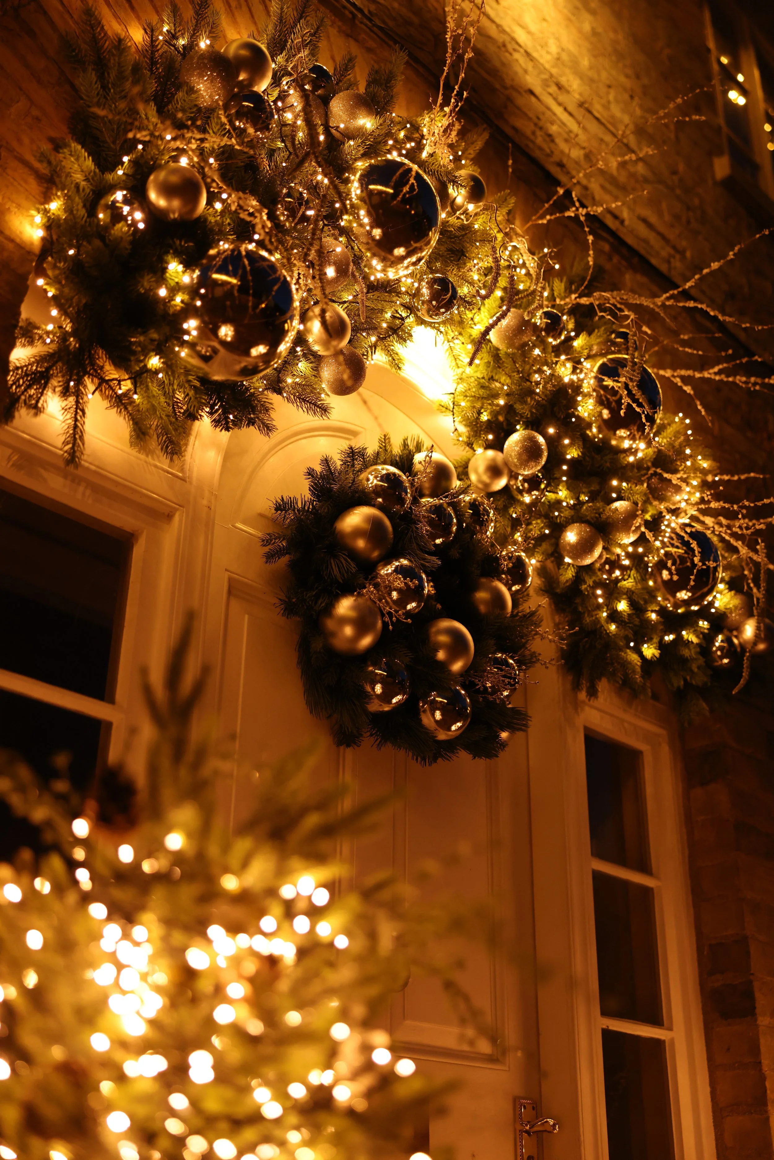 Decorated Christmas arch with silver chrome baubles and warm lights framing a doorway at night.