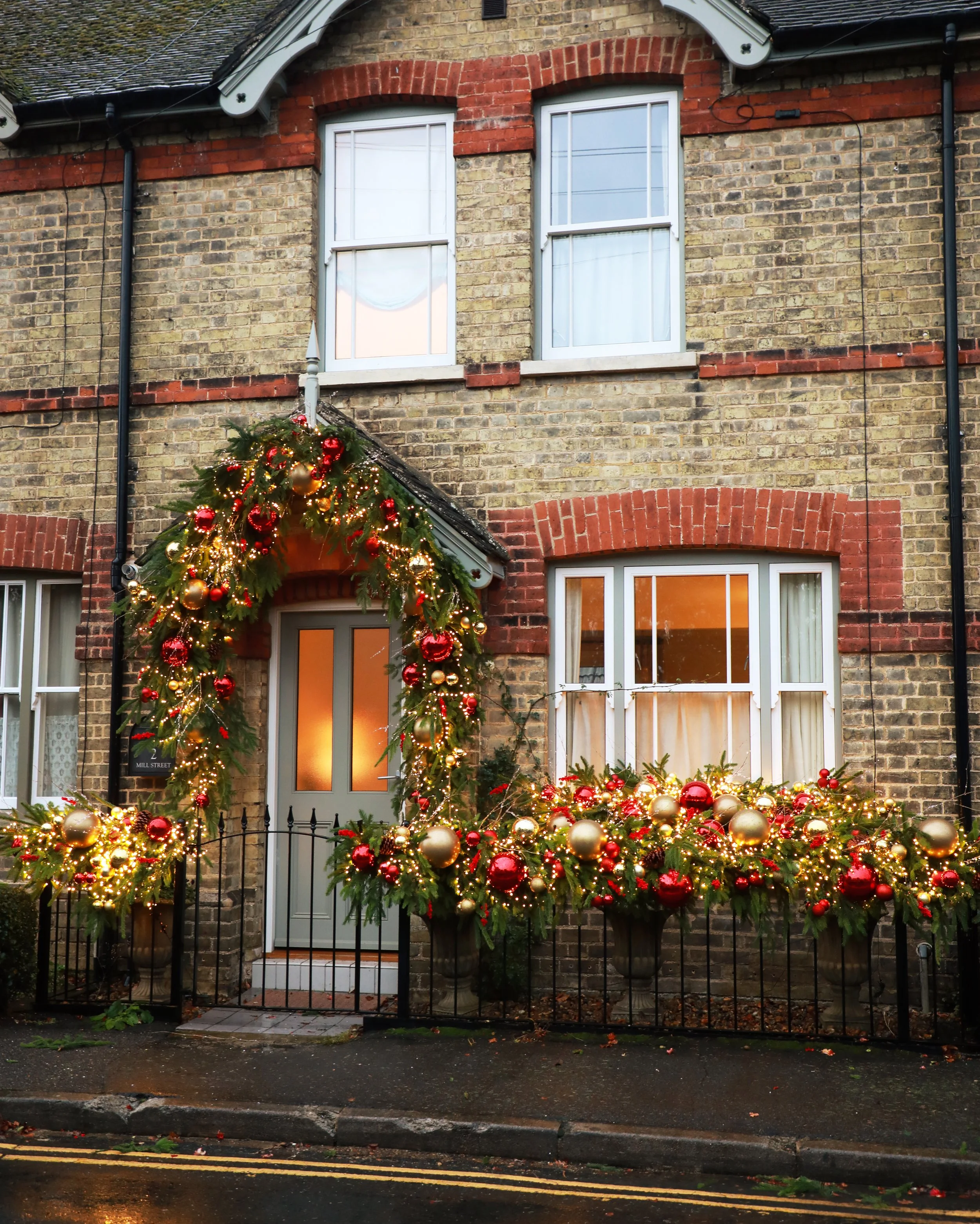 A decorated house with Christmas garlands and ornaments around the door and windows, illuminated by string lights.