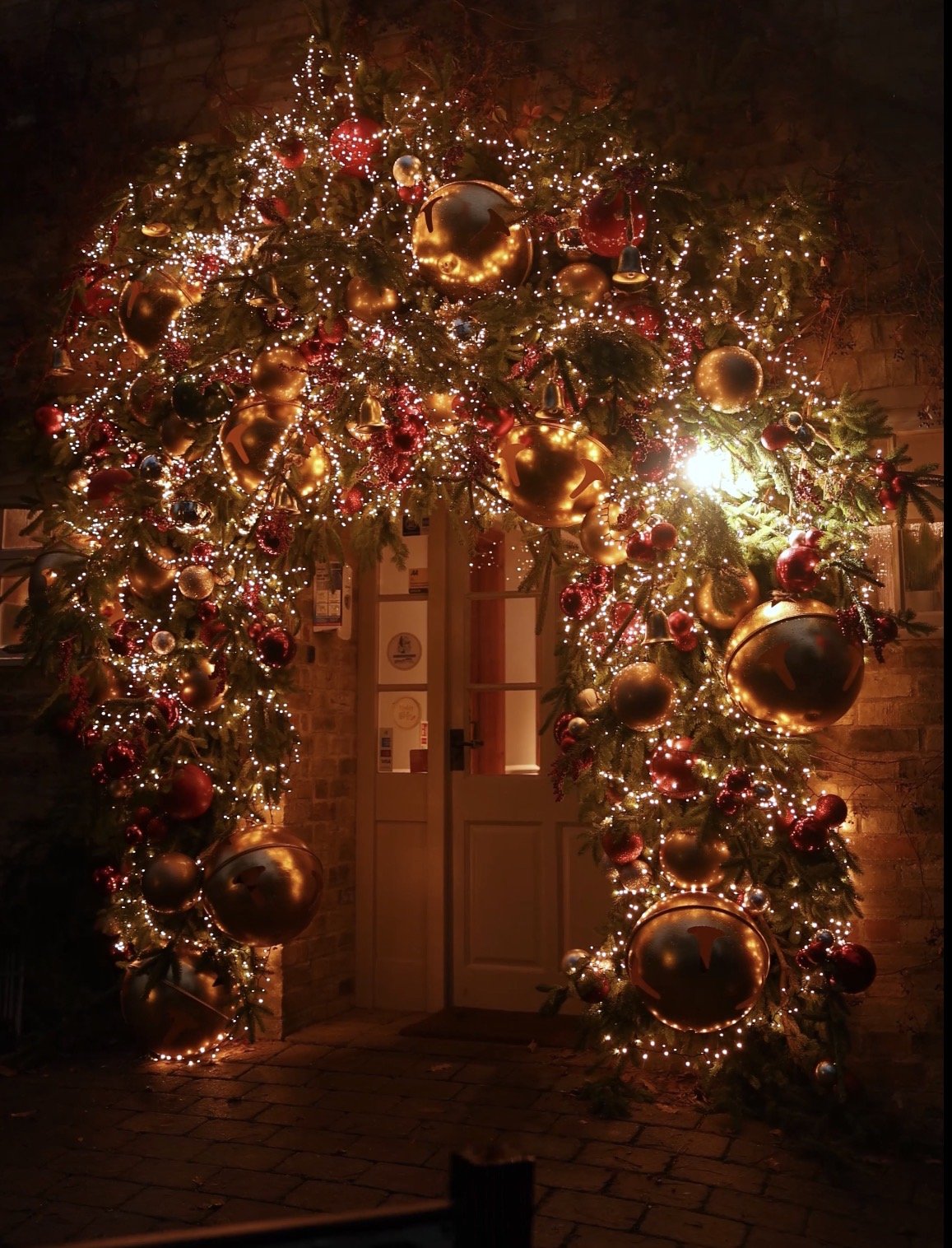 A nutcracker Christmas | A festive Christmas arch decorated with gold, red, and silver ornaments, oversized bells, glittering lights, and greenery, framing a doorway. 