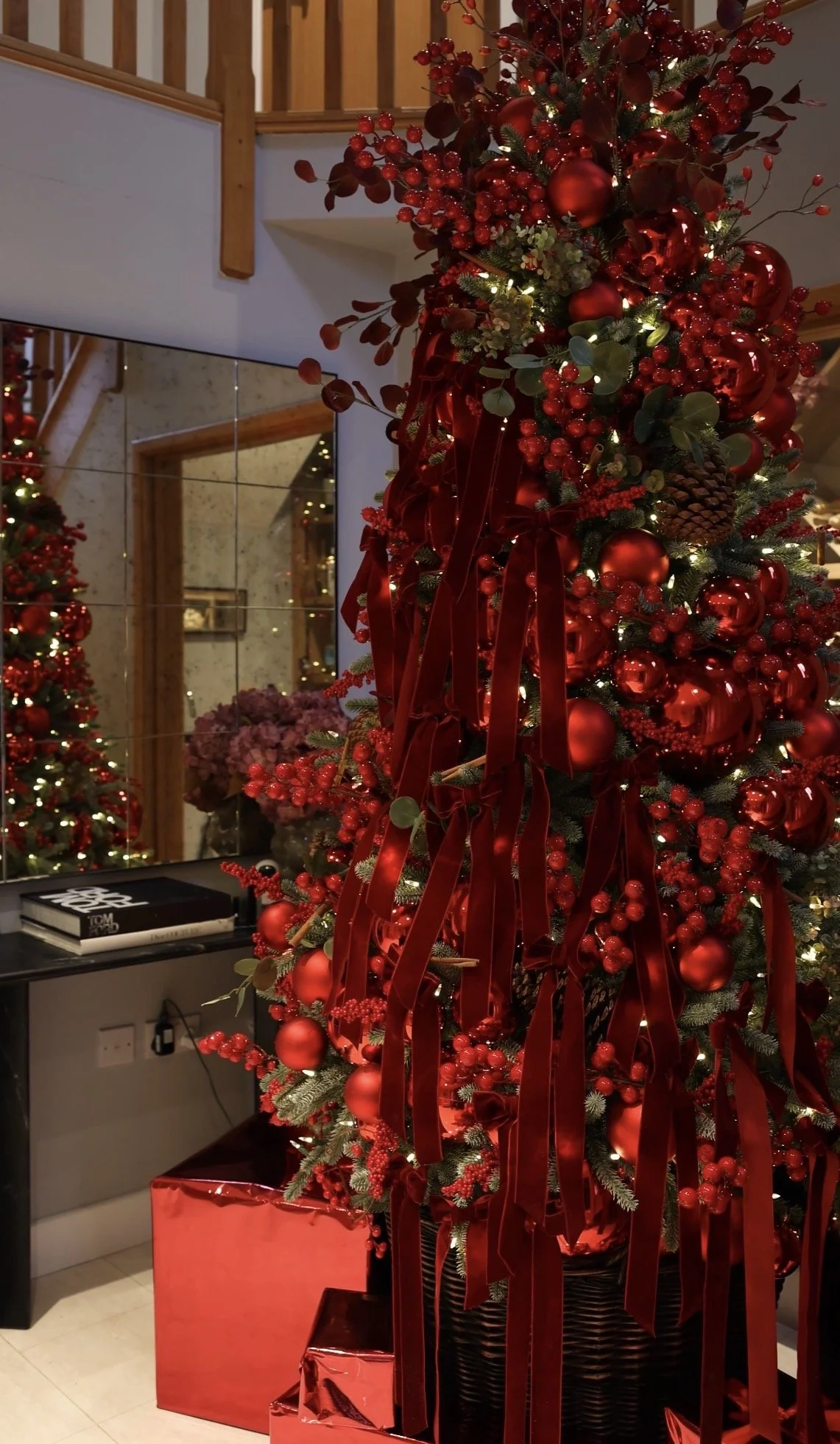 Decorated Christmas tree with red ornaments, ribbons, pinecones, and lights, placed in a Christmas-themed setting with gift boxes underneath.