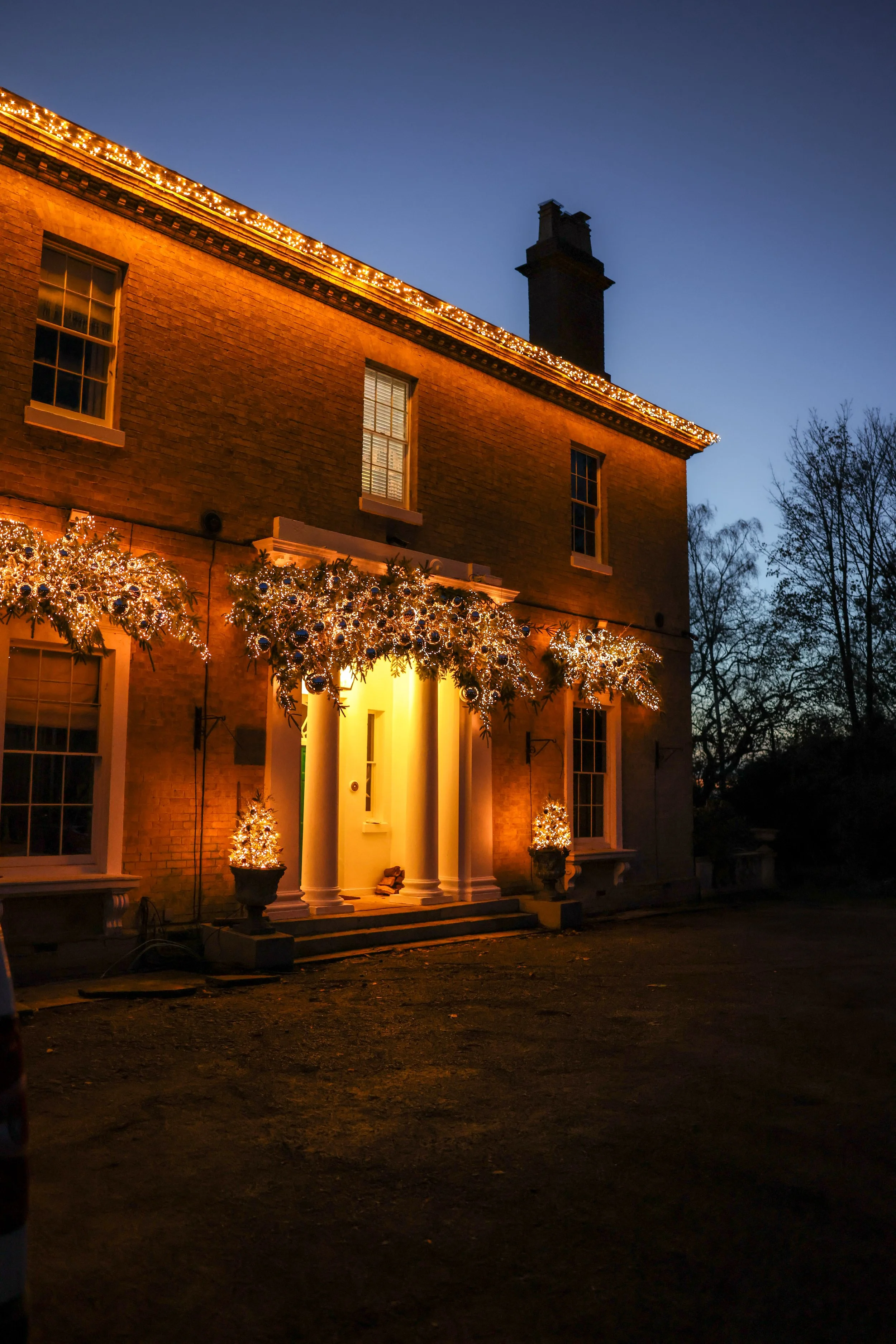 A large brick house decorated with Christmas lights and ornaments, with a dark blue evening sky in the background.