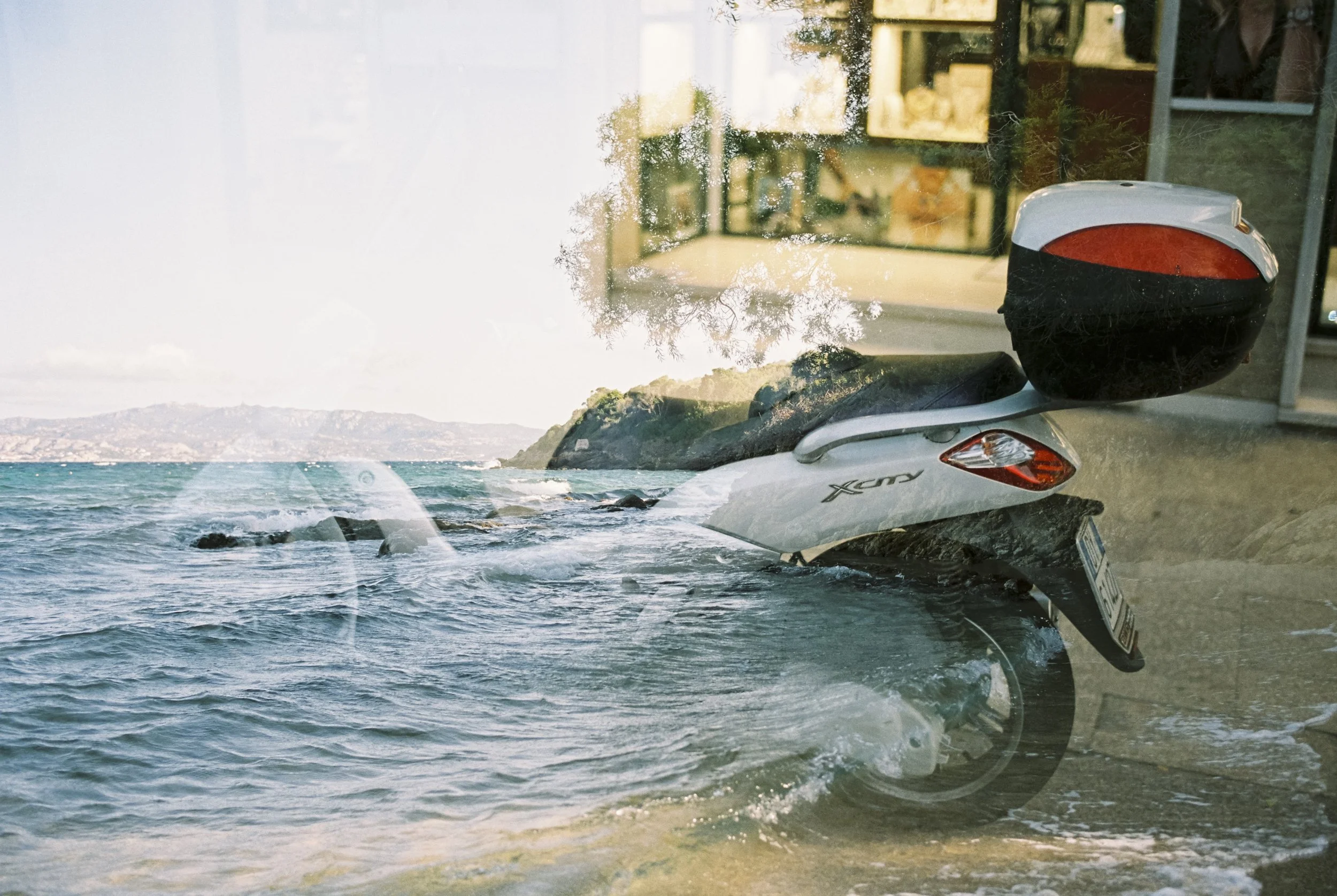 Ein Bild einer Scooter, das vor einem Meeresblick durch eine Glasfensterscheibe fotografiert wurde.