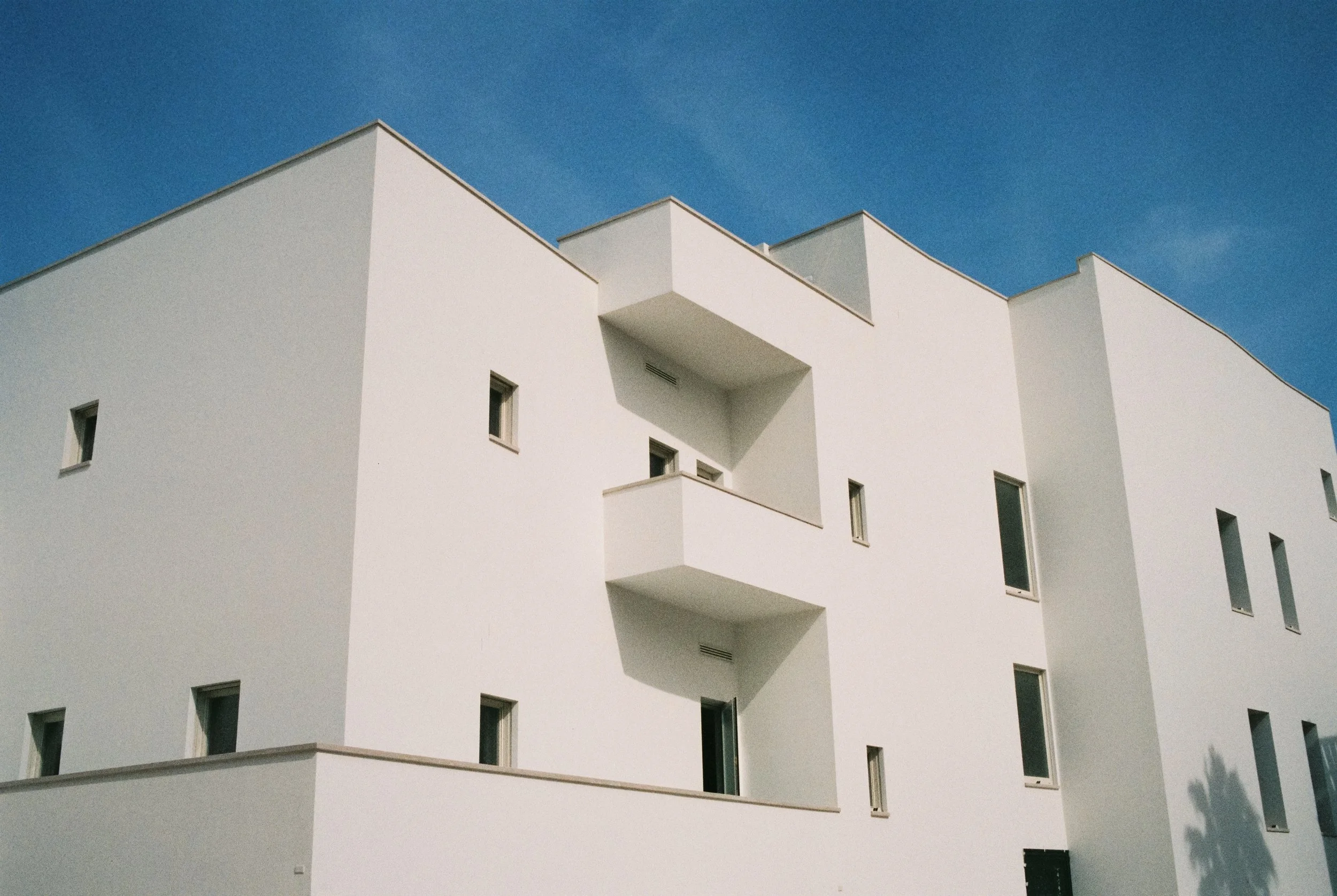 Moderne weiße Wohngebäude mit eckigen Balkonen gegen blauen Himmel.