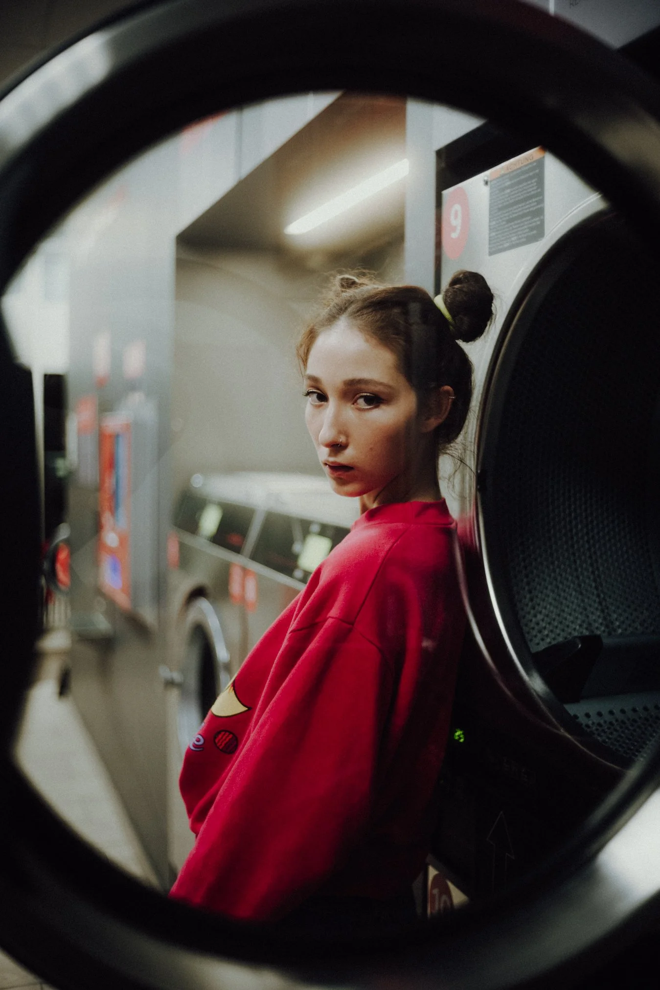 Eine junge Frau in einem roten Pullover schaut durch die Öffnung einer Waschmaschine in einer Wäscherei.