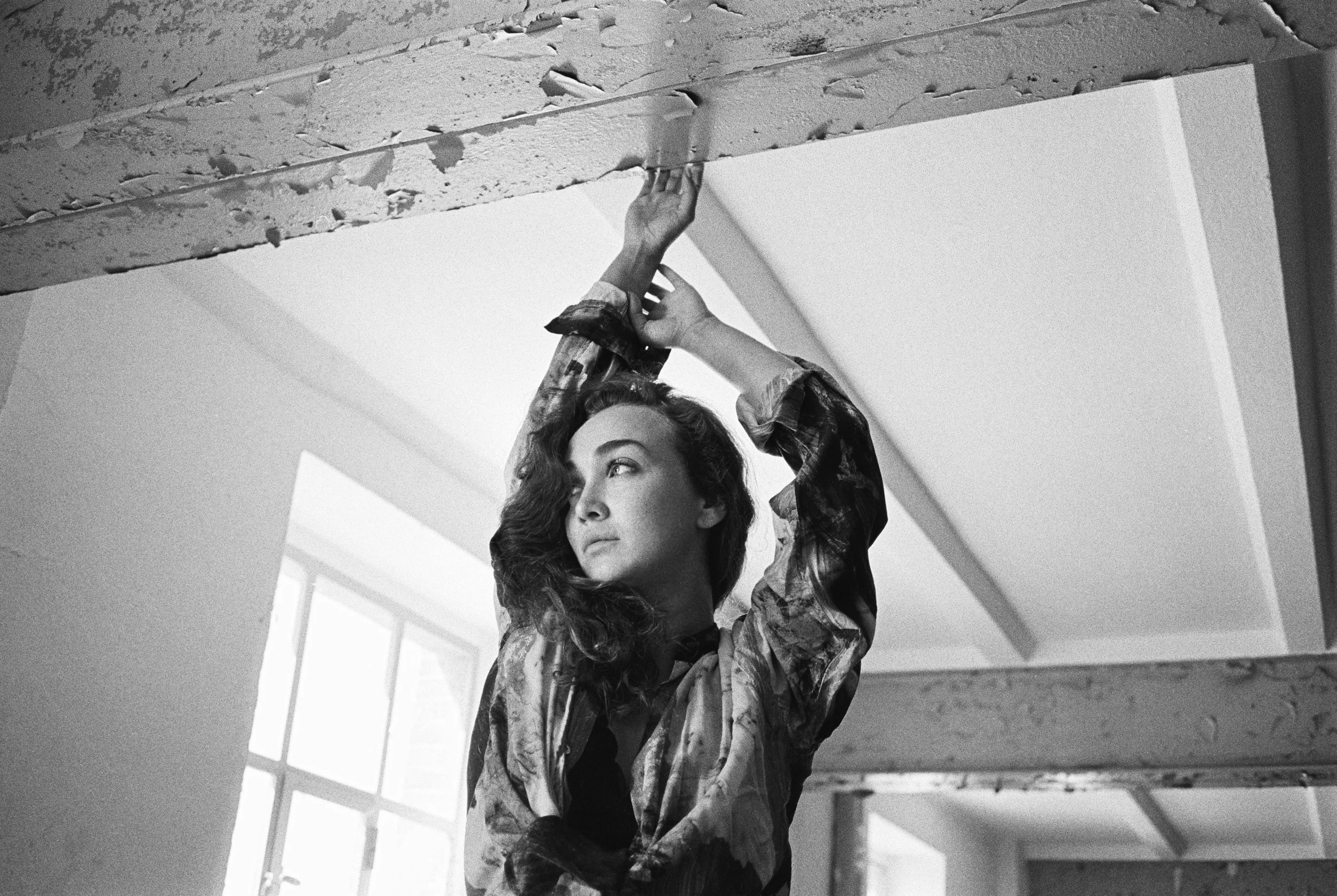 Eine junge Frau mit dunklen, gewellten Haaren hängt an einer Decke und schaut nach oben.