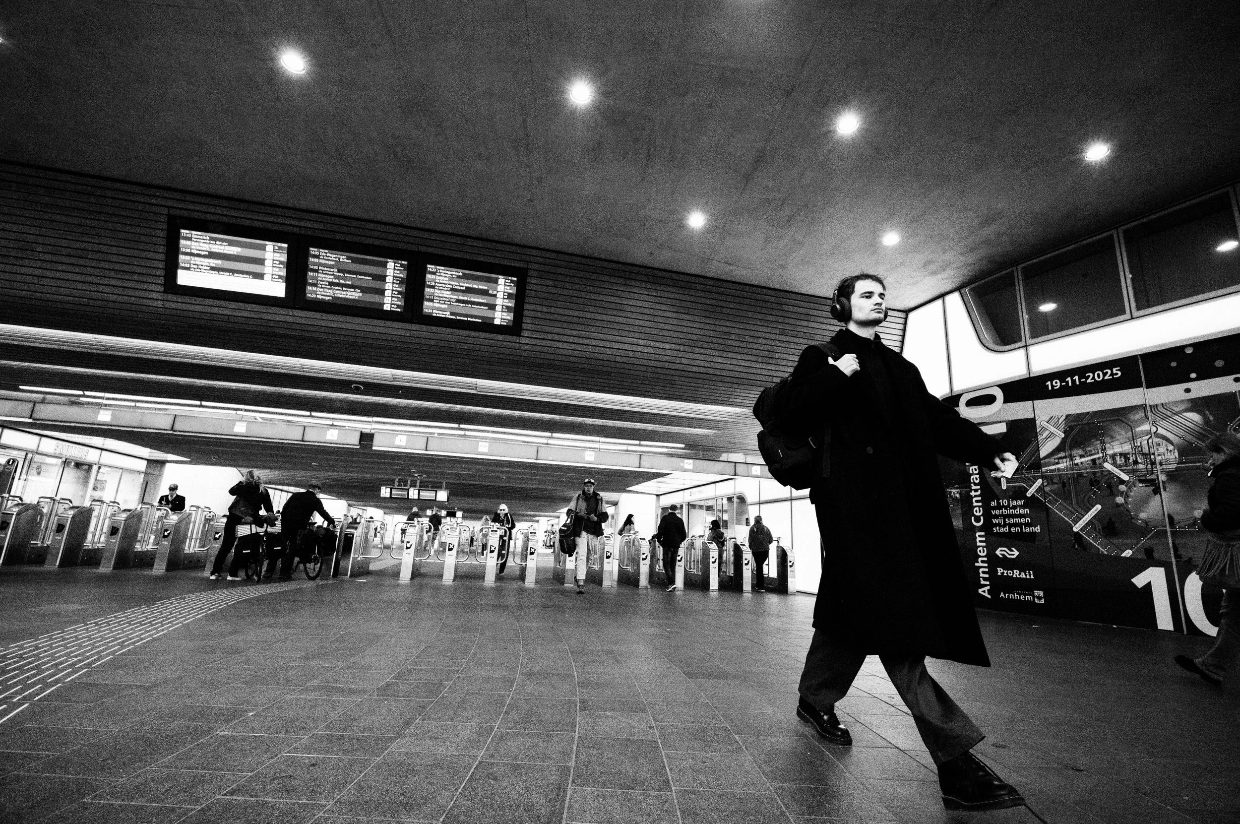 Schwarz-weiß-Foto eines Bahnhofs mit Menschen, die durch die Eingangstüren gehen, und einem Fahrkartenautomaten.