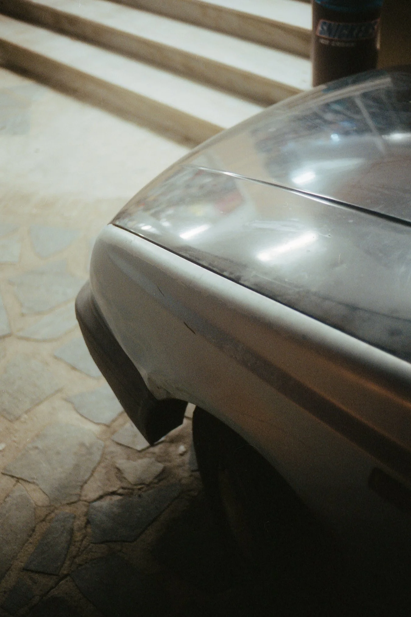 Nahaufnahme des Vorderendes eines abgestellten Autos, sichtbar sind die Motorhaube und die vordere Stoßstange im Haus- oder Garagenbereich.
