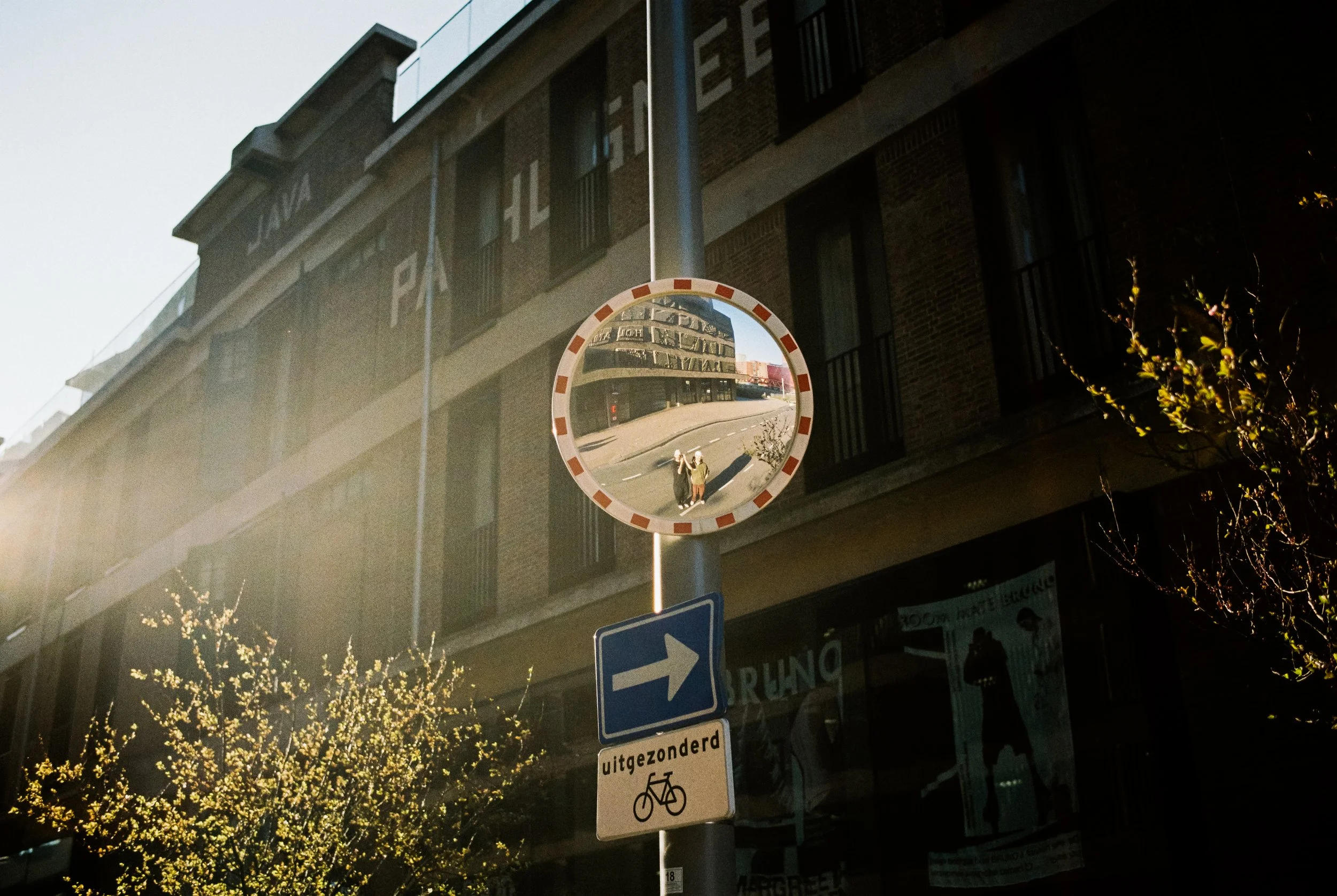 Spiegel am Straßenrand reflektiert die umgebende Stadt und die Person, die das Foto macht, mit einem Gebäude im Hintergrund.