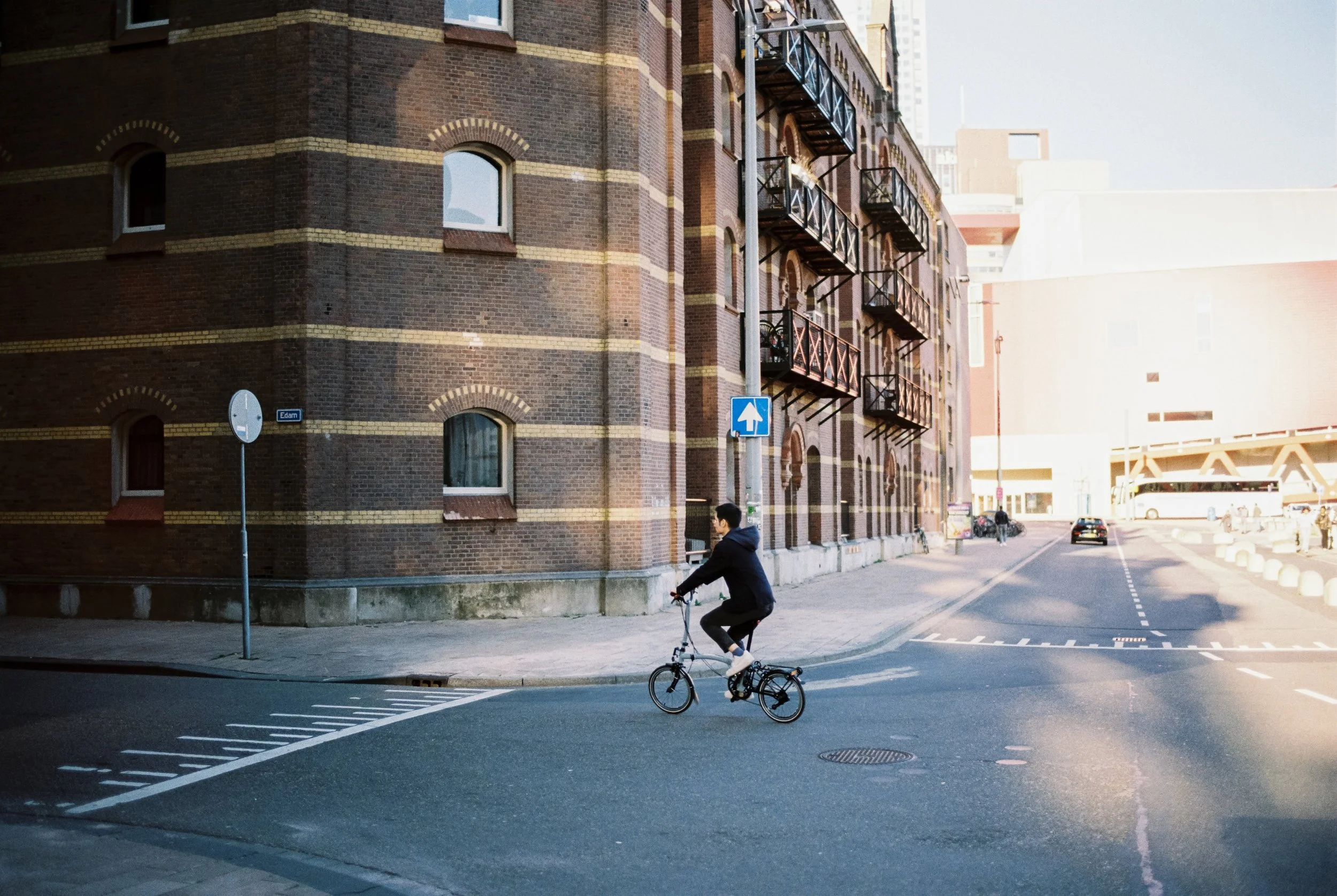 Junge Person fährt Fahrrad auf der Straße in einer Stadt, umgeben von Backsteingebäuden und modernen Gebäuden im Hintergrund.